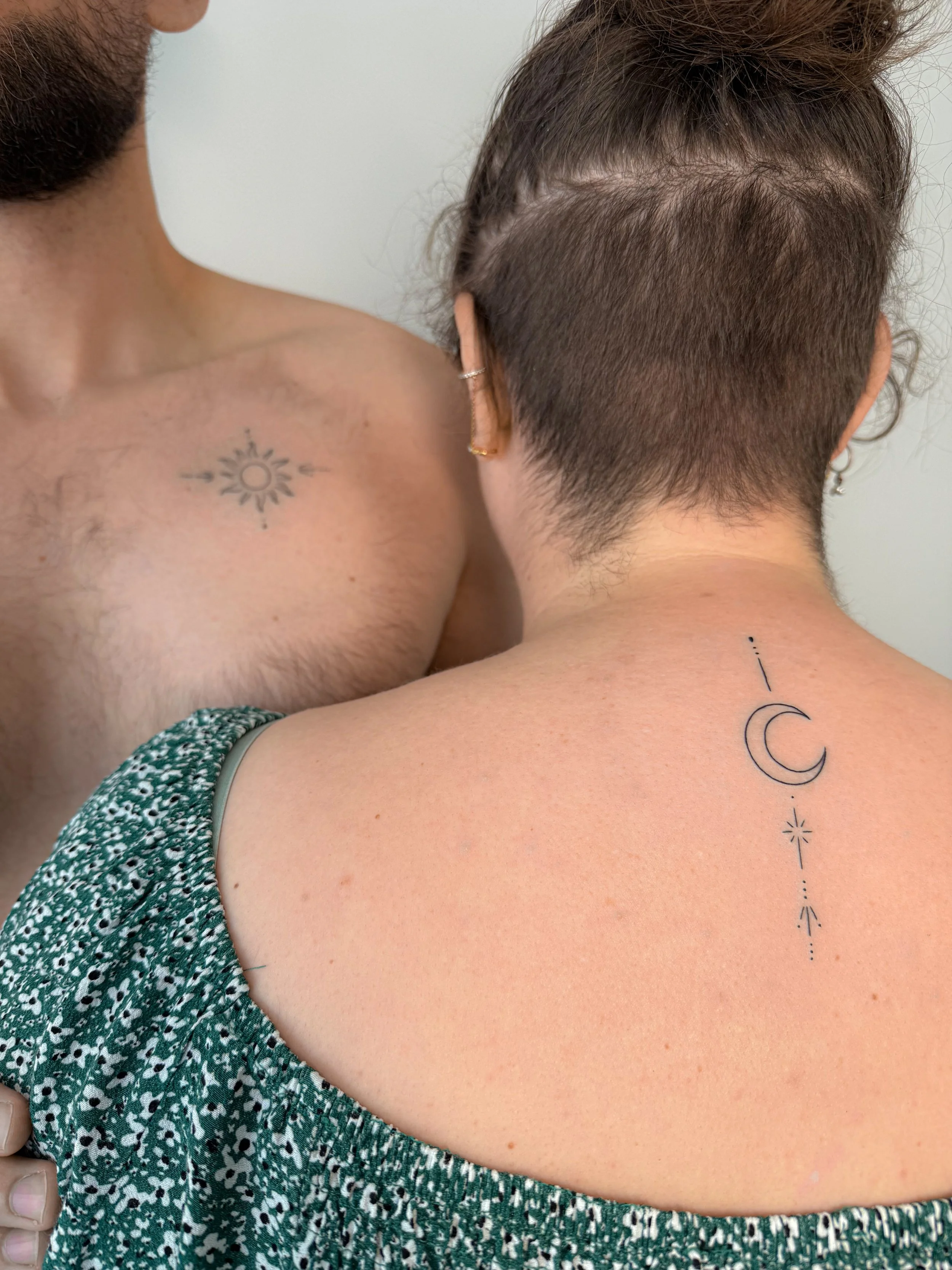 Close-up van een persoon met kort haar en een tattoo op de nek, naast een andere persoon met een tattoo op de borst.