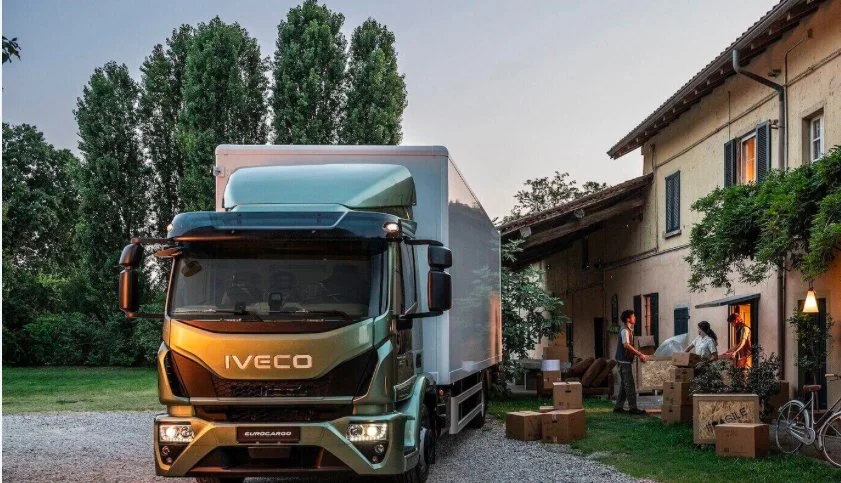 Iveco Eurocargo truck parked outside a house as people unload boxes.