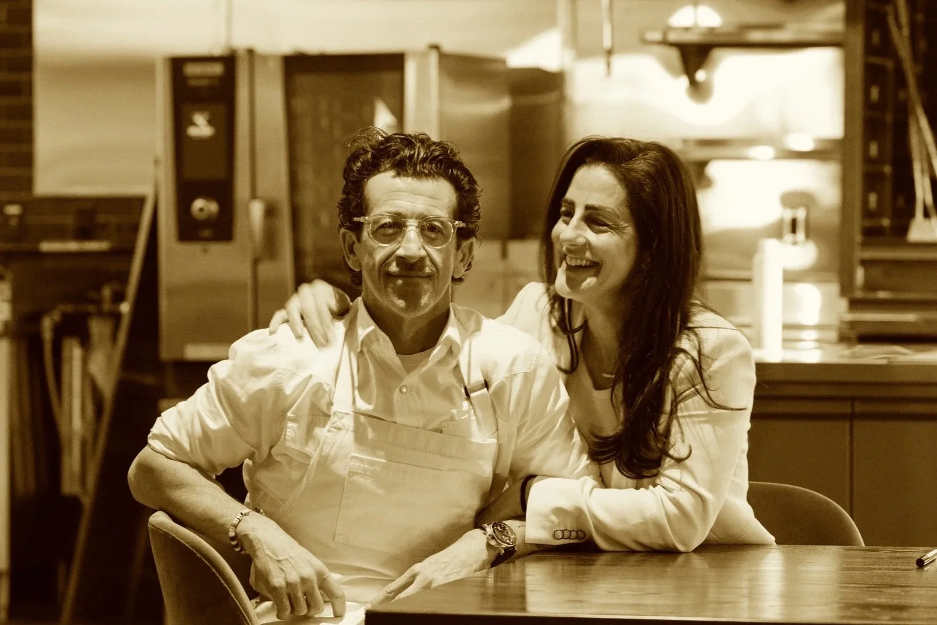 Chef Robbie Wilson and Emily Perry Wilson sitting together at a table in a kitchen, smiling.