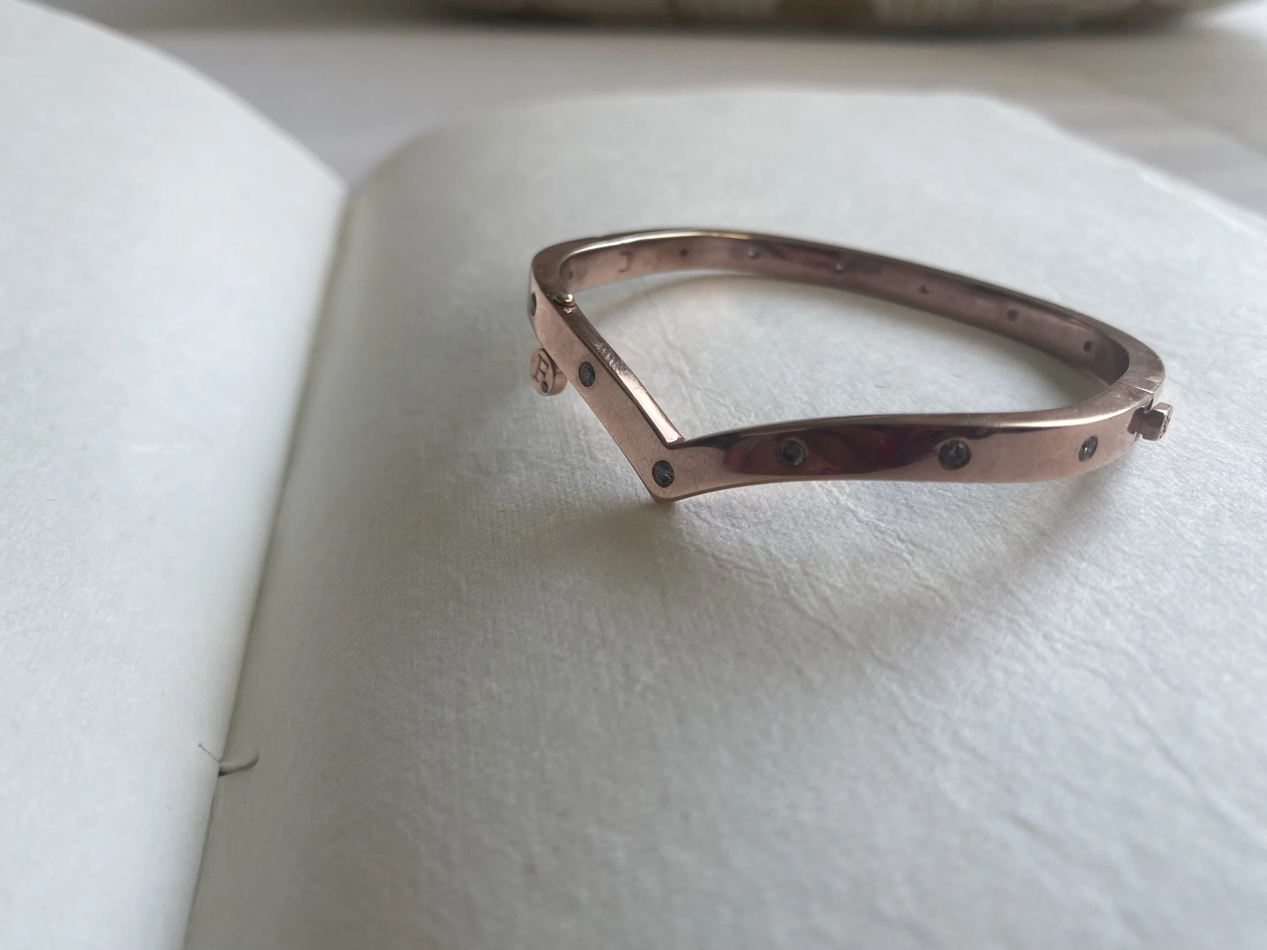 Close-up of a rose gold bracelet with small gray stones, resting on a white textured surface within an open light-colored notebook.