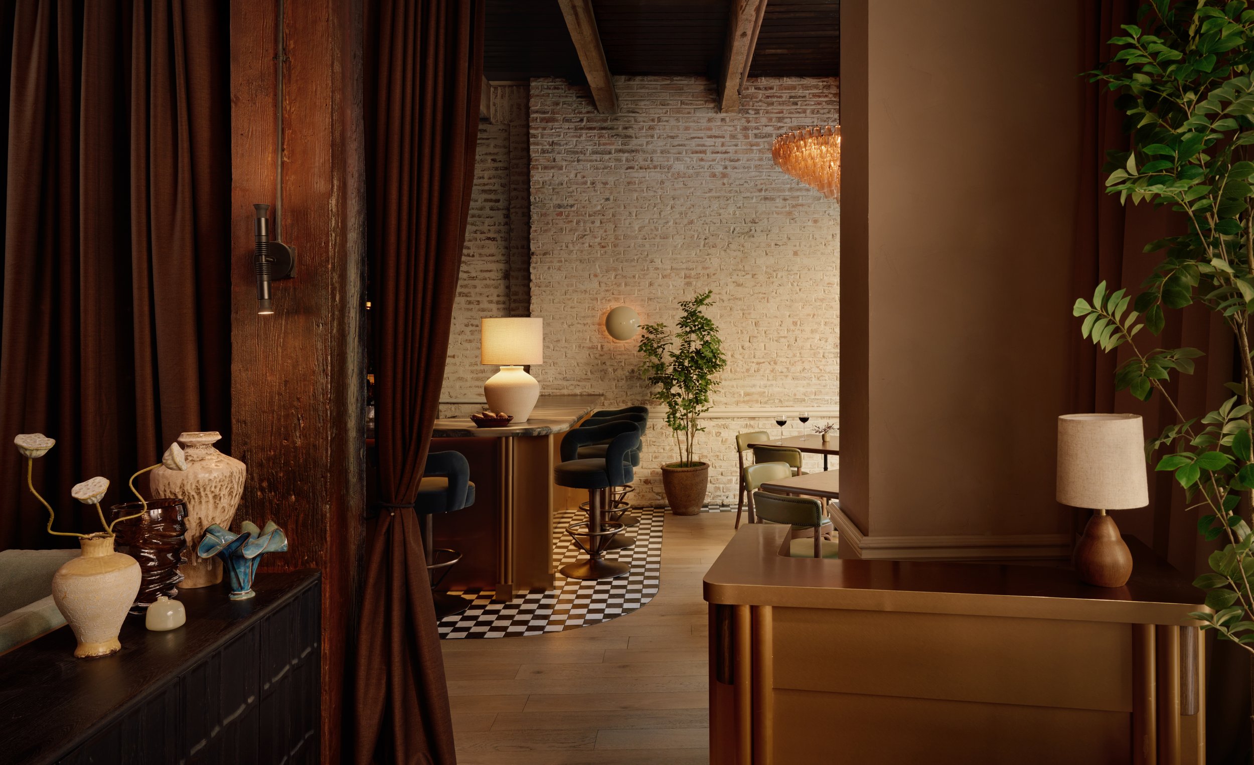 Interior of a modern bar with a long marble counter, barstools, a TV screen showing a basketball game, and shelves with bottles of liquor. Warm lighting and wooden ceiling beams create a cozy atmosphere.
