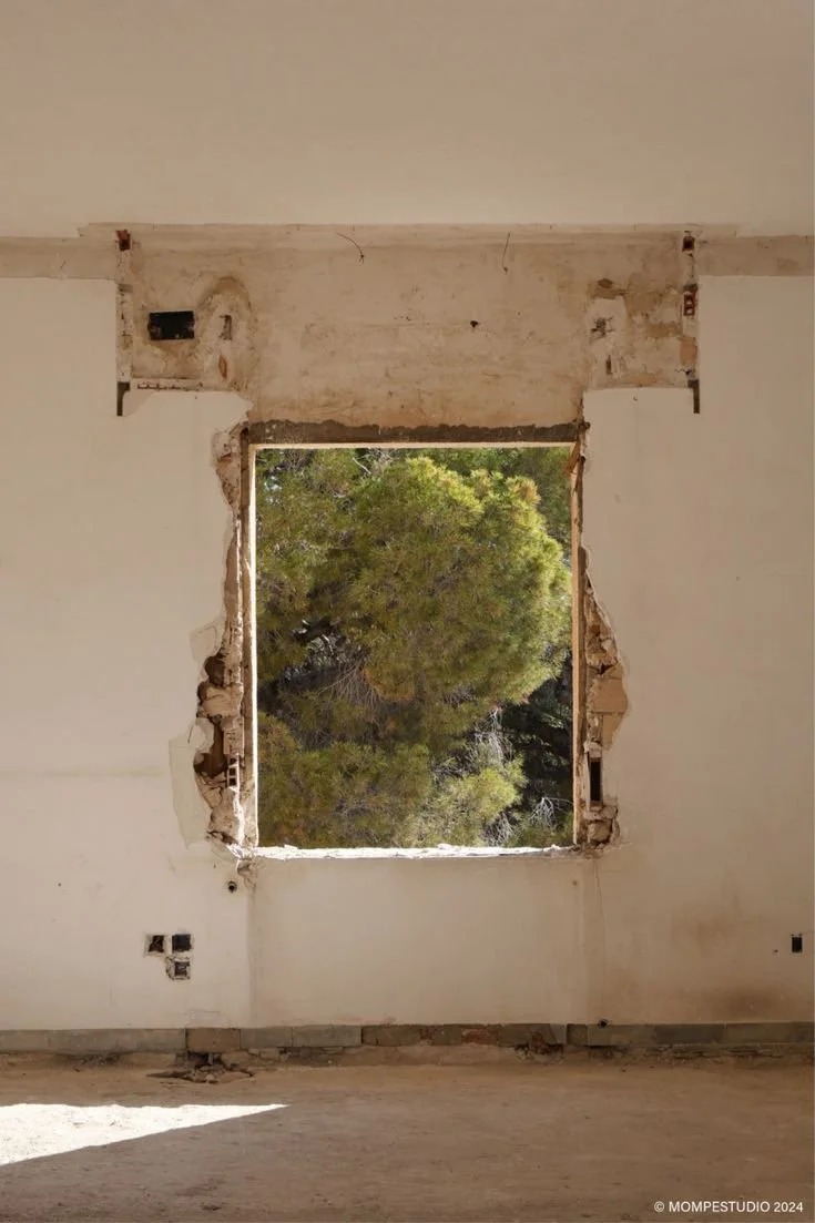 Empty room with a large rectangular hole in the wall revealing green trees outside.