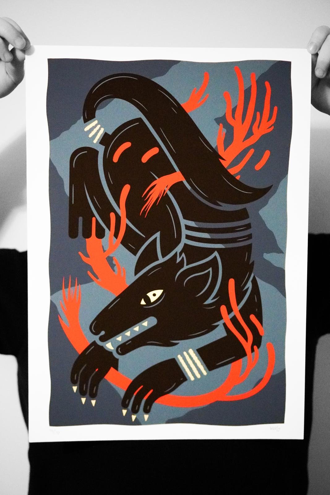 A person holding a colorful illustration of a mythical creature with a wolf's head and body, flames, and stylized horns or hair, depicted in bold black, red, and gray tones.