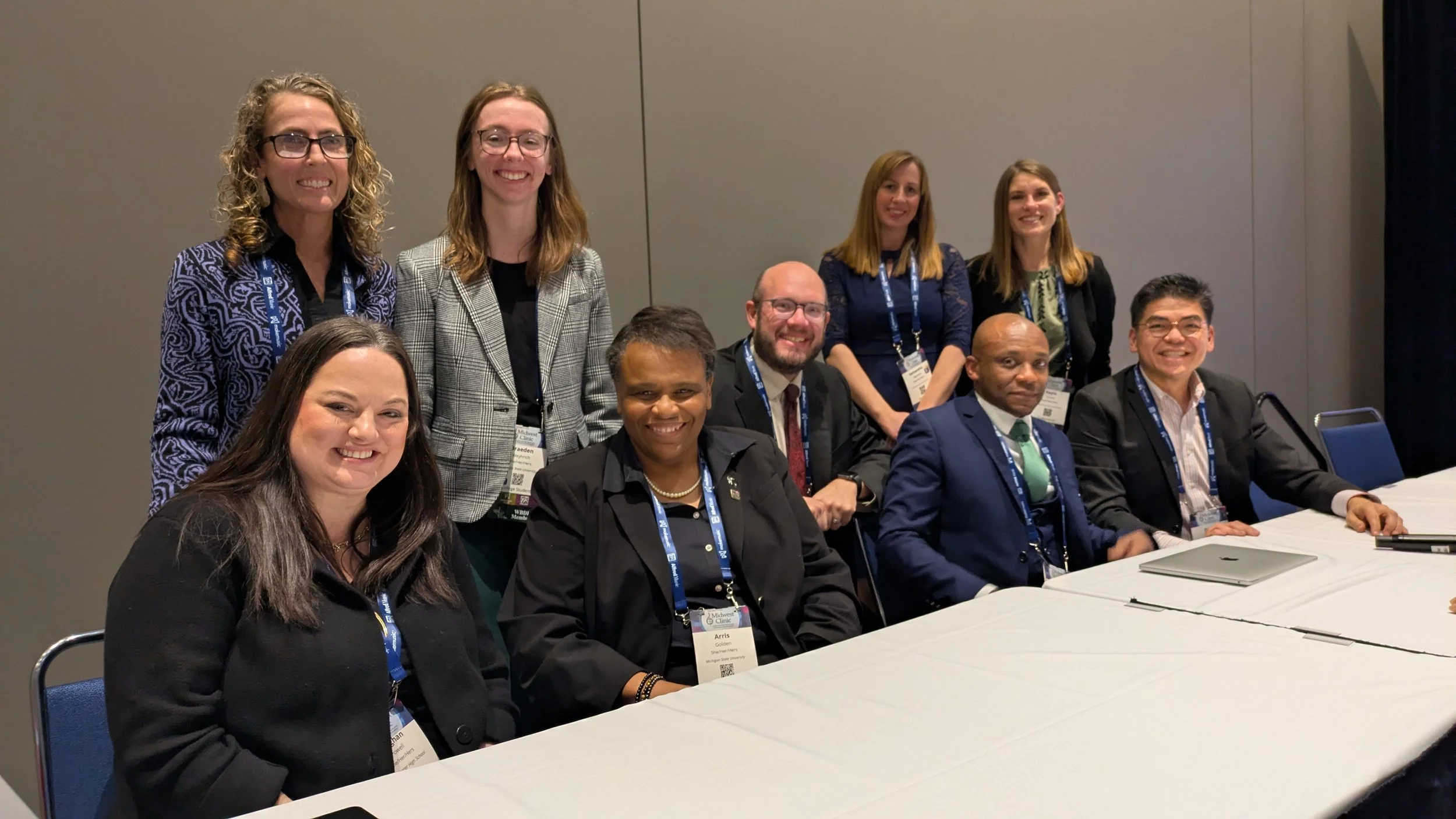 A group of smiling music educators, of varying ages, genders, and races, in professional clothing at a conference.