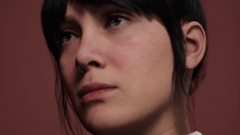 Close-up of a young person with short dark hair and fair skin, looking slightly to the side against a plain background.