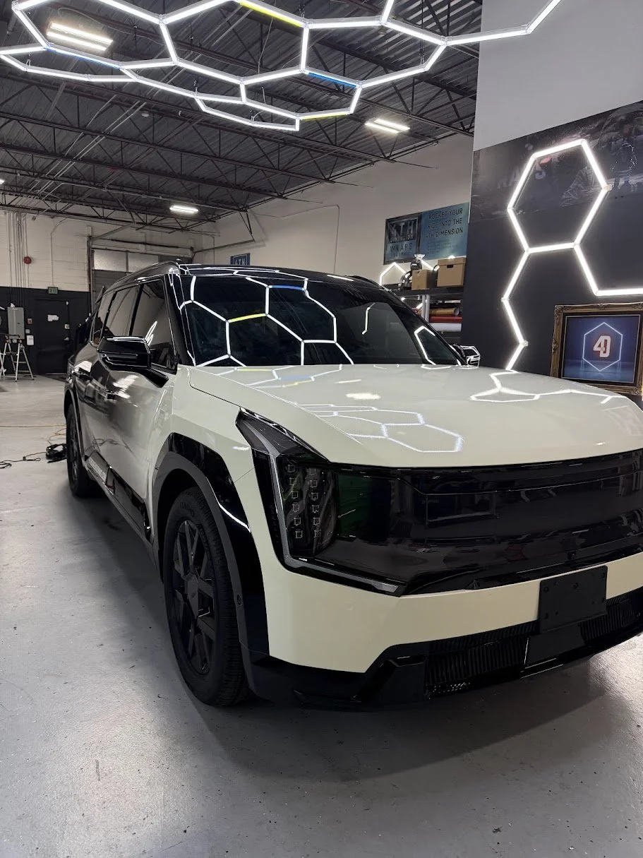 A white and black electric vehicle inside a showroom or workshop, with hexagonal LED light fixtures on the ceiling and wall.