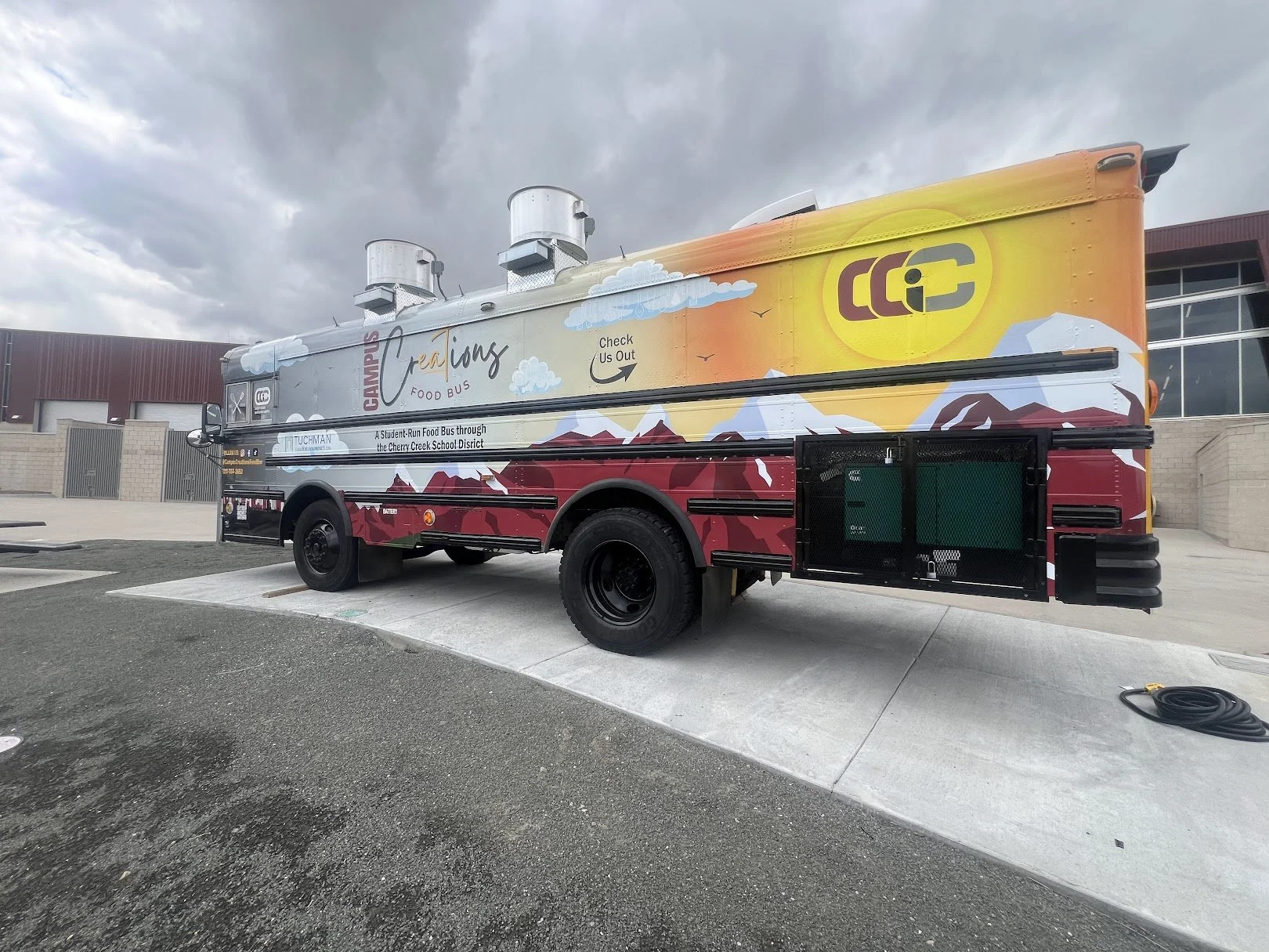 A colorful food truck labeled 'Campbell's Creations Food Bus' parked outside under dark cloudy skies.