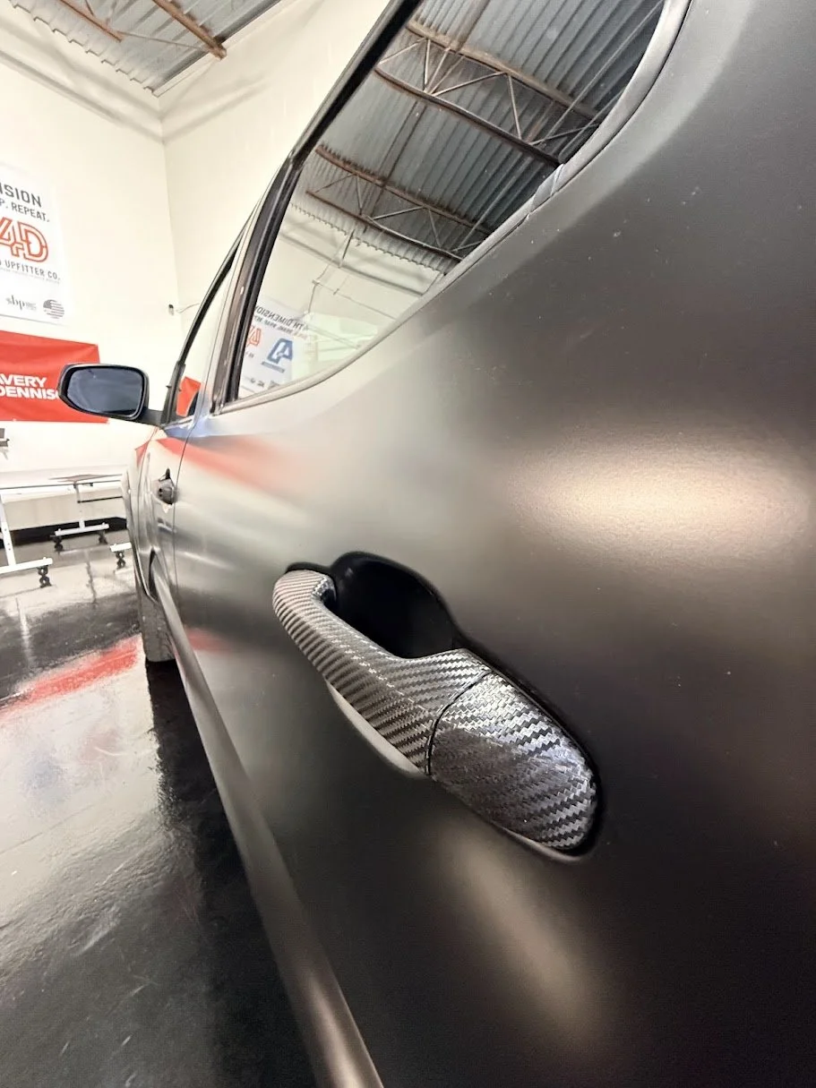 Close-up of a car door handle with a carbon fiber design inside an indoor garage.