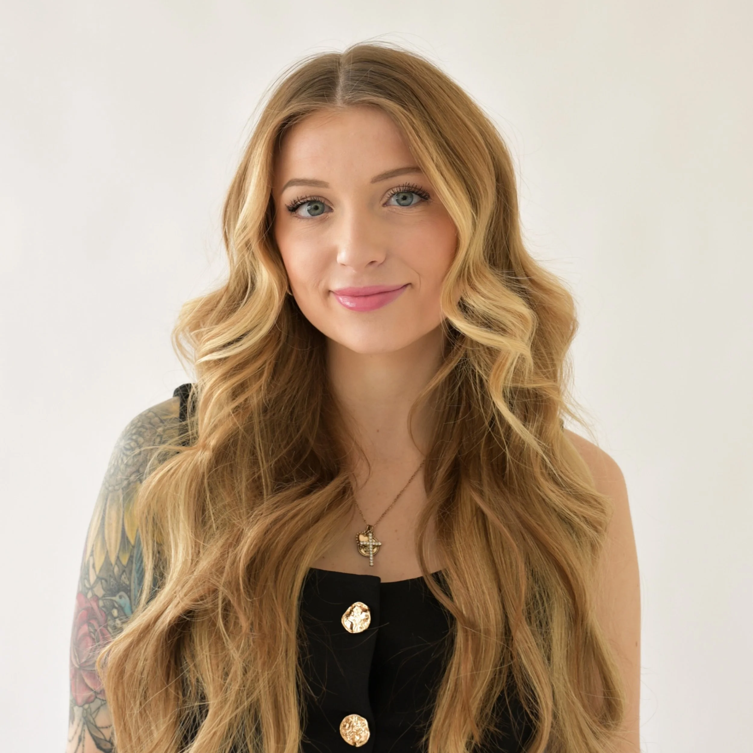 Woman in a white sweater and blue jeans smiling against a plain background.