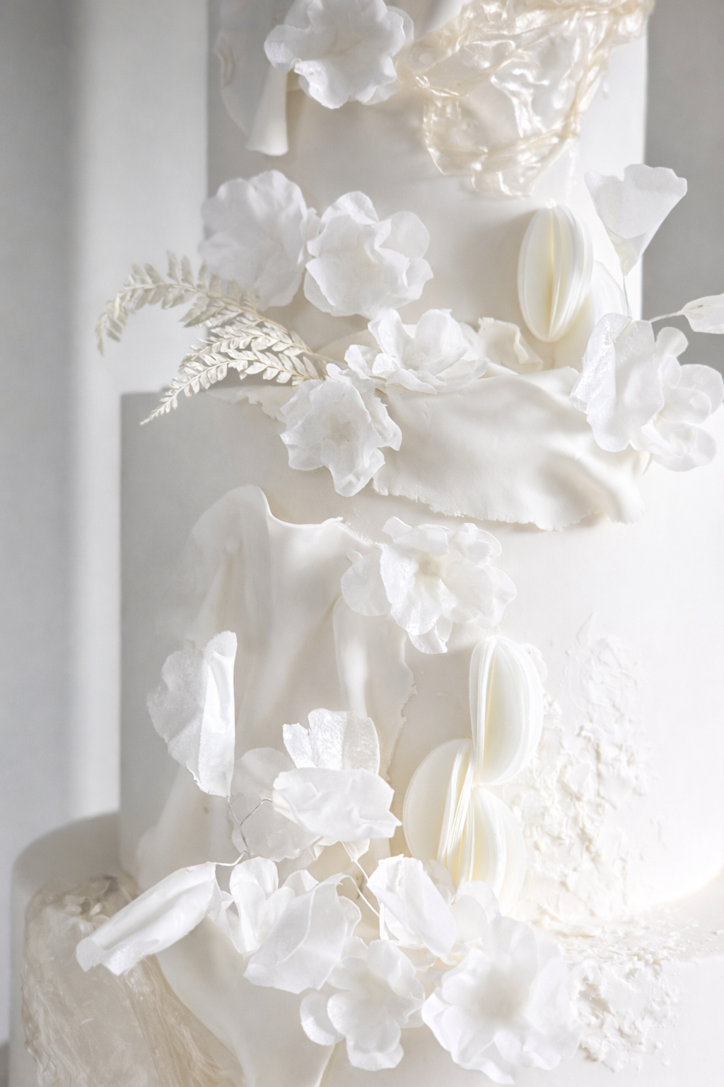 Close-up of a white wedding cake decorated with white flowers, leaves, and elegant white chocolate accents.