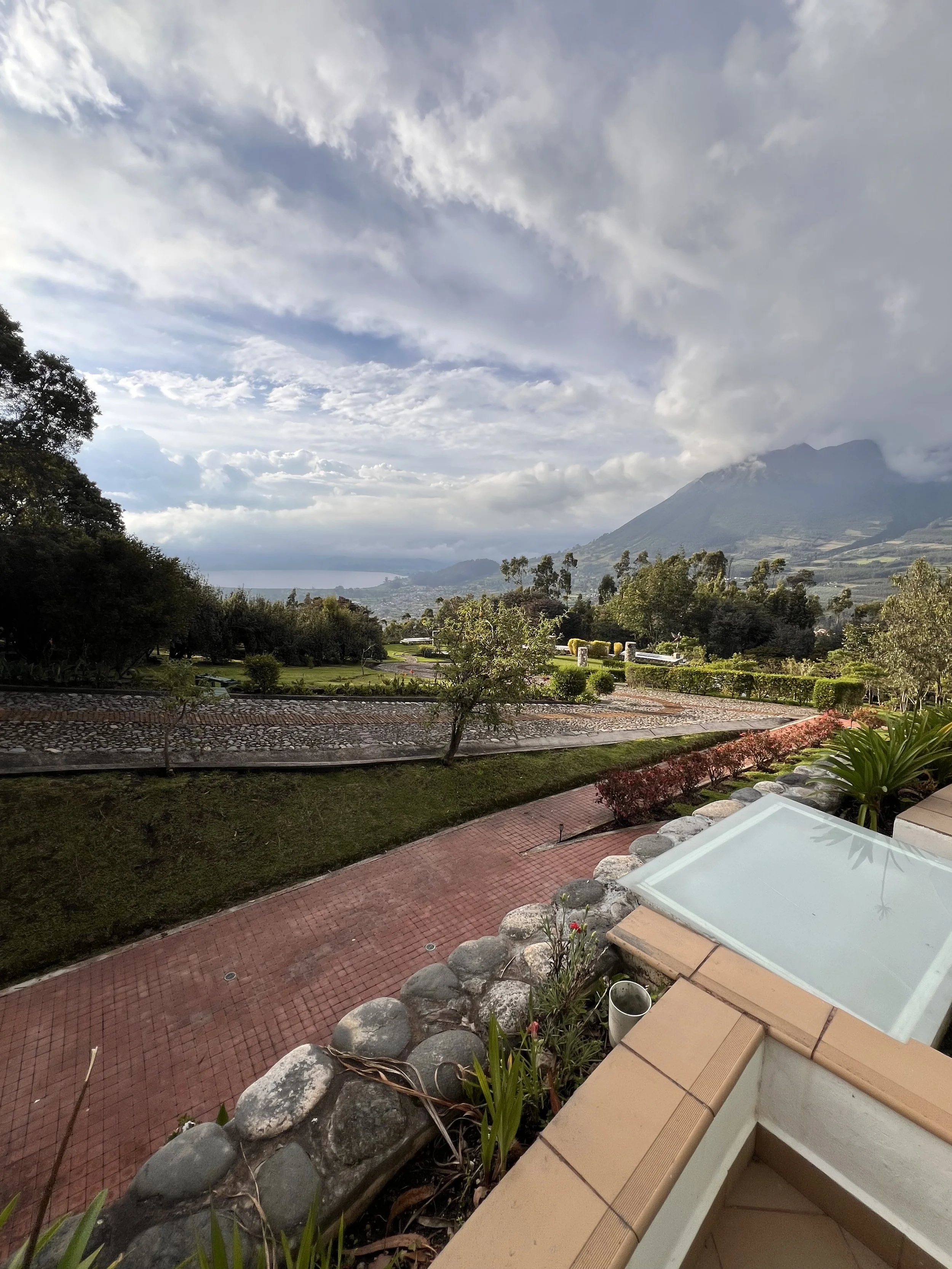 Scenic view of a mountain with clouds, a church, and well-maintained gardens and pathways in a rural landscape.