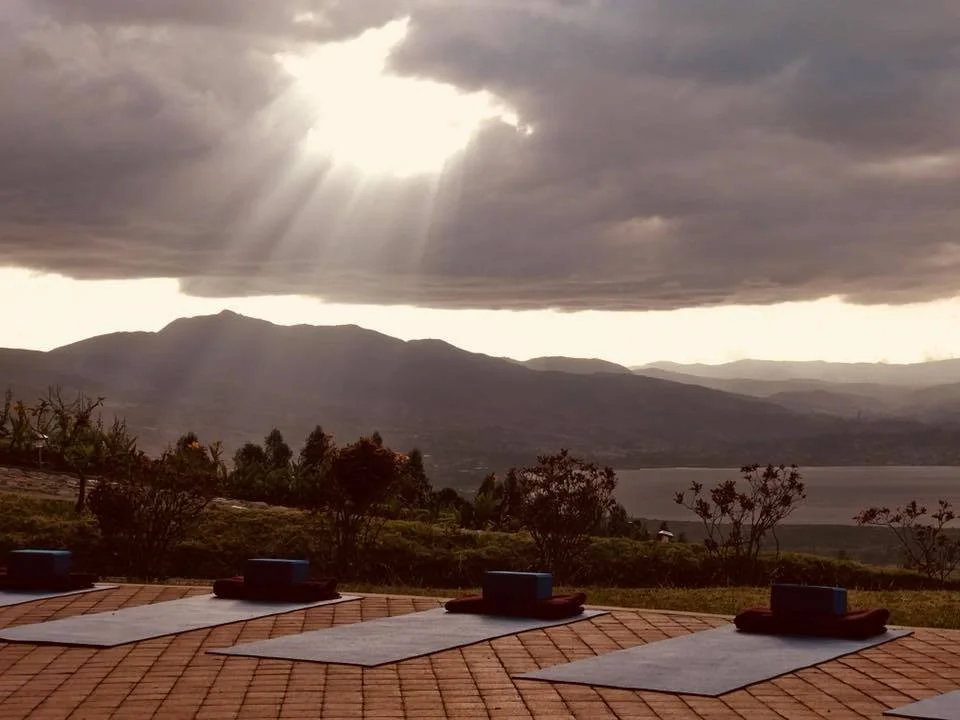 Yoga mats on a tiled roof overlooking a lake, mountains, and cloudy sky with sun rays coming through the clouds.