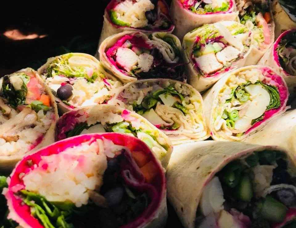 Close-up of assorted fresh vegetable and chicken wraps sliced in half, showing lettuce, chicken, blueberries, and other vegetables.