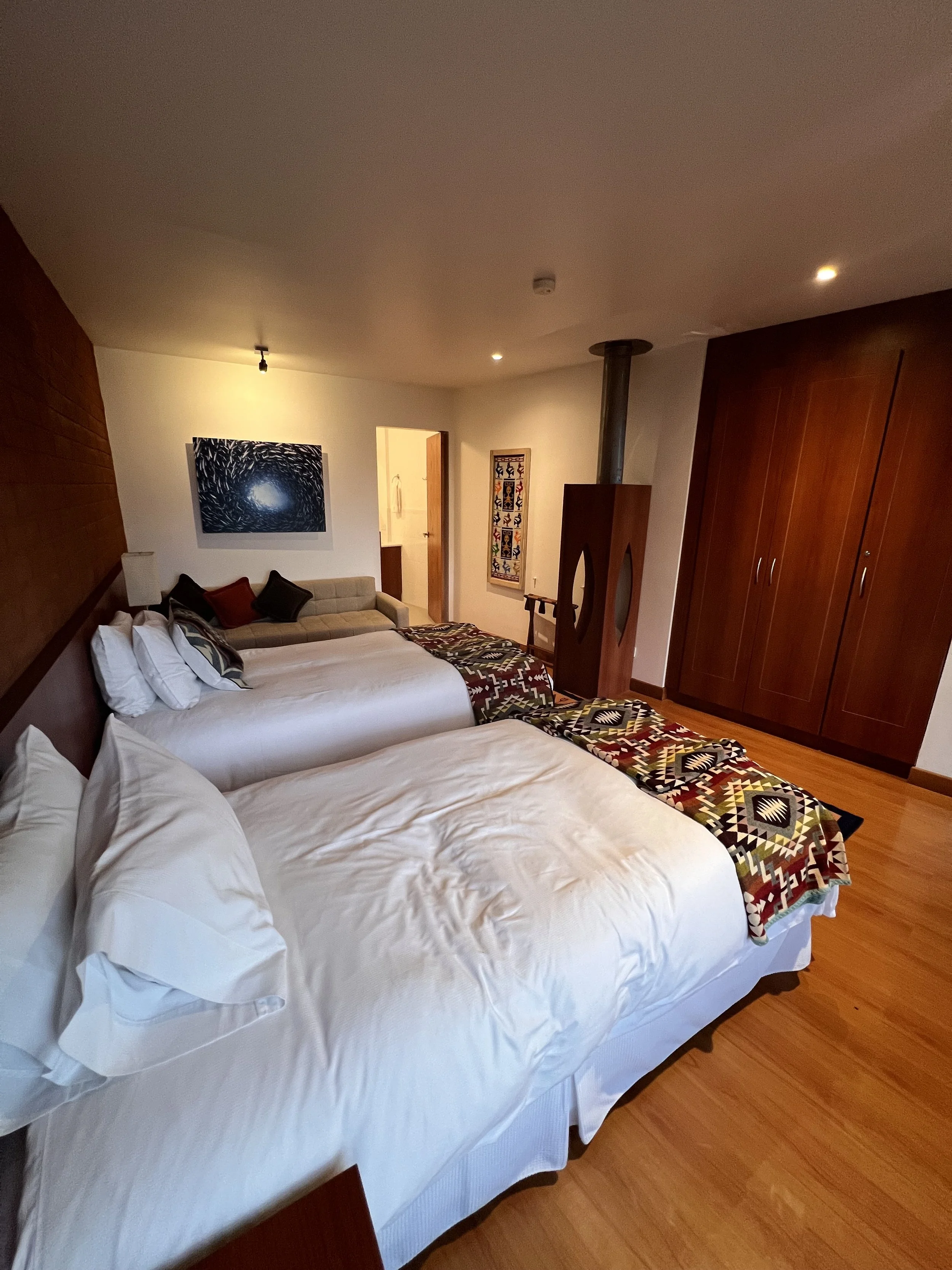 A hotel room with two twin beds, a wooden wardrobe, a patterned bed runner, and artwork on the wall.