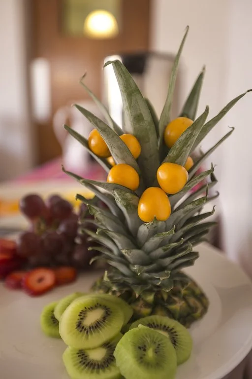 Decorative arrangement of a pineapple with yellow berries and sliced kiwi on a white plate.