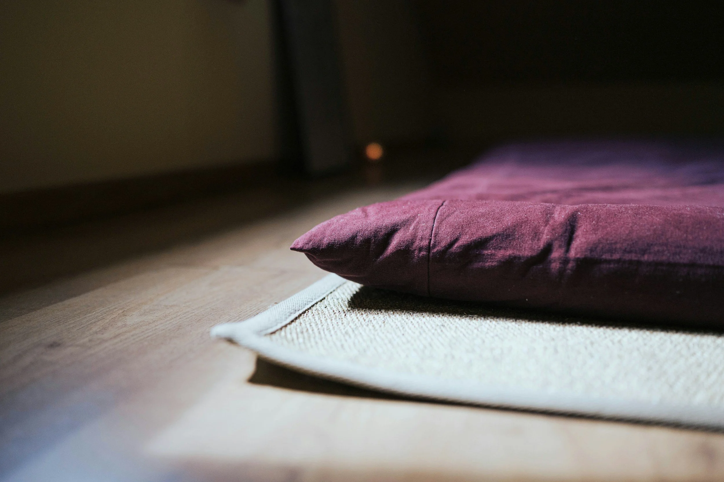 Purple Thai massage mat resting on a beige woven mat on a wooden floor, with a shadowed background.