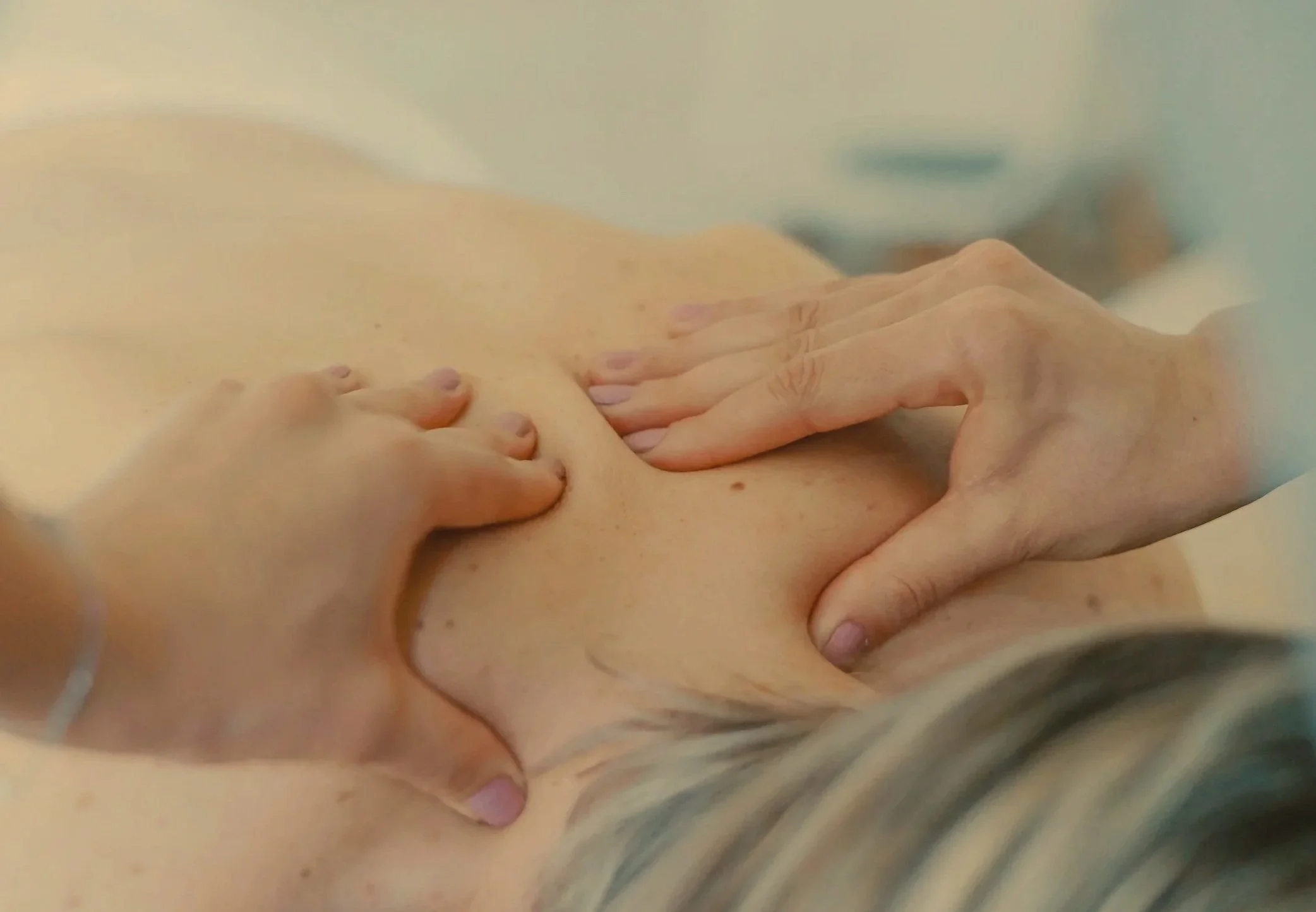 Close-up of a person's upper back and neck during a massage, with massage therapist's hands applying pressure.