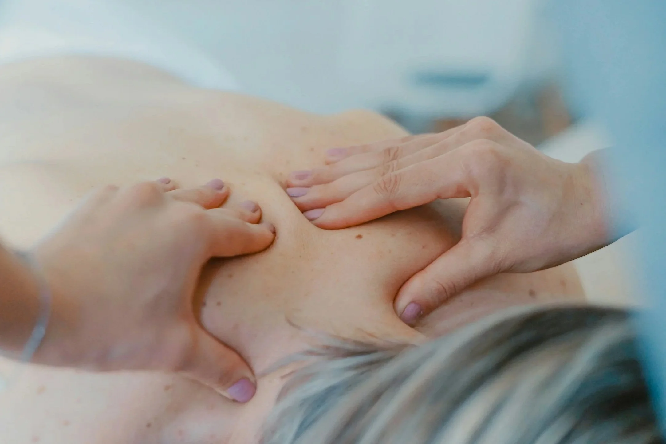 Close-up of a person's upper back and neck during a massage, with massage therapist's hands applying pressure.