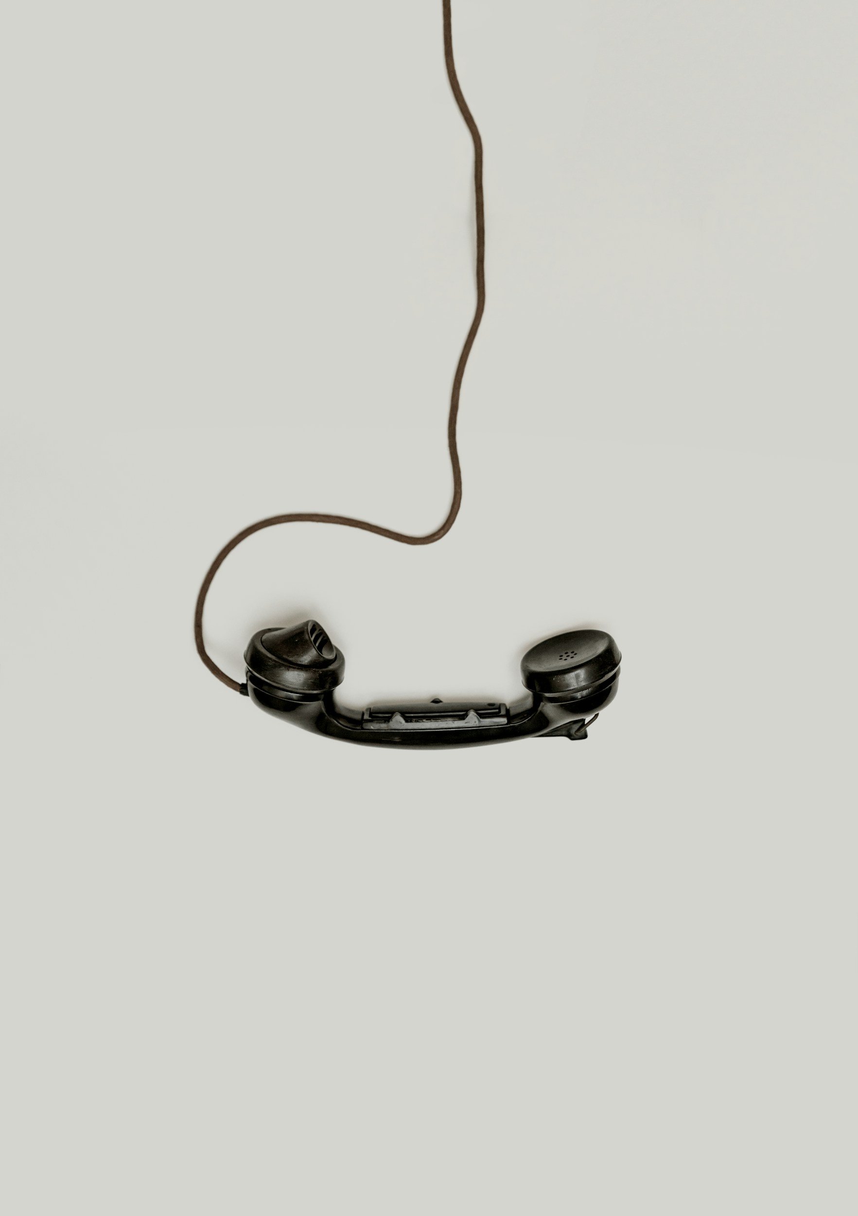 Old black landline telephone with a cord hang on a plain light background.
