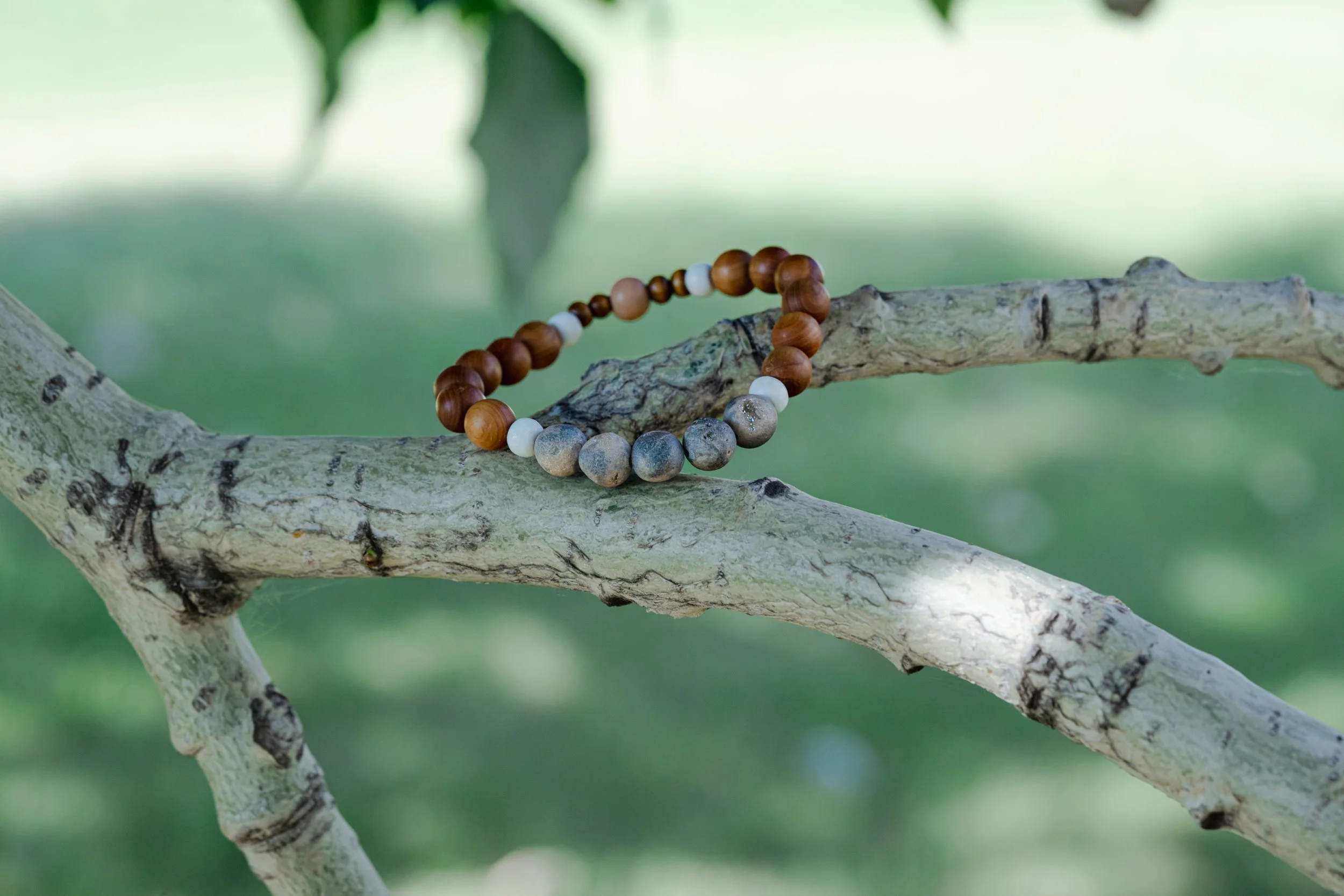 A beaded bracelet resting on a tree branch outdoors with a green, blurred background.