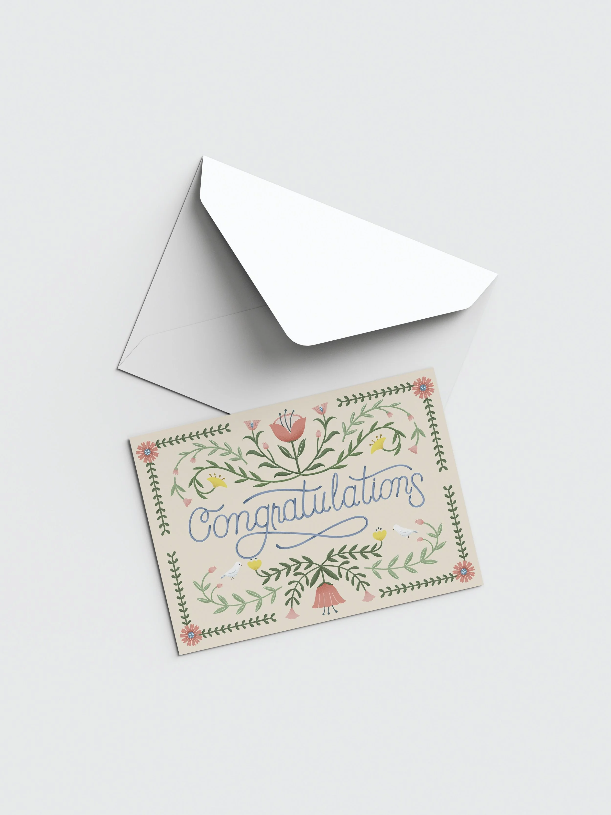A greeting card with floral design and the word 'Congratulations' on it, placed beside a white envelope on a white surface.