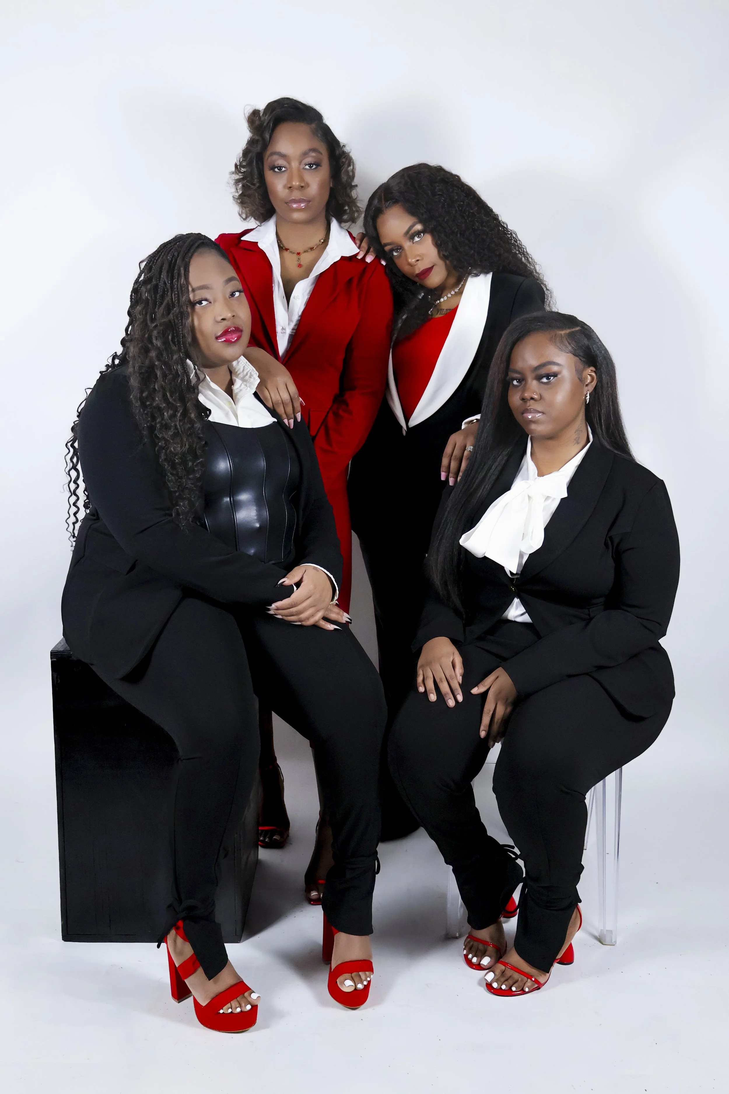 Five women dressed in black and white with red accents pose together against a white backdrop.