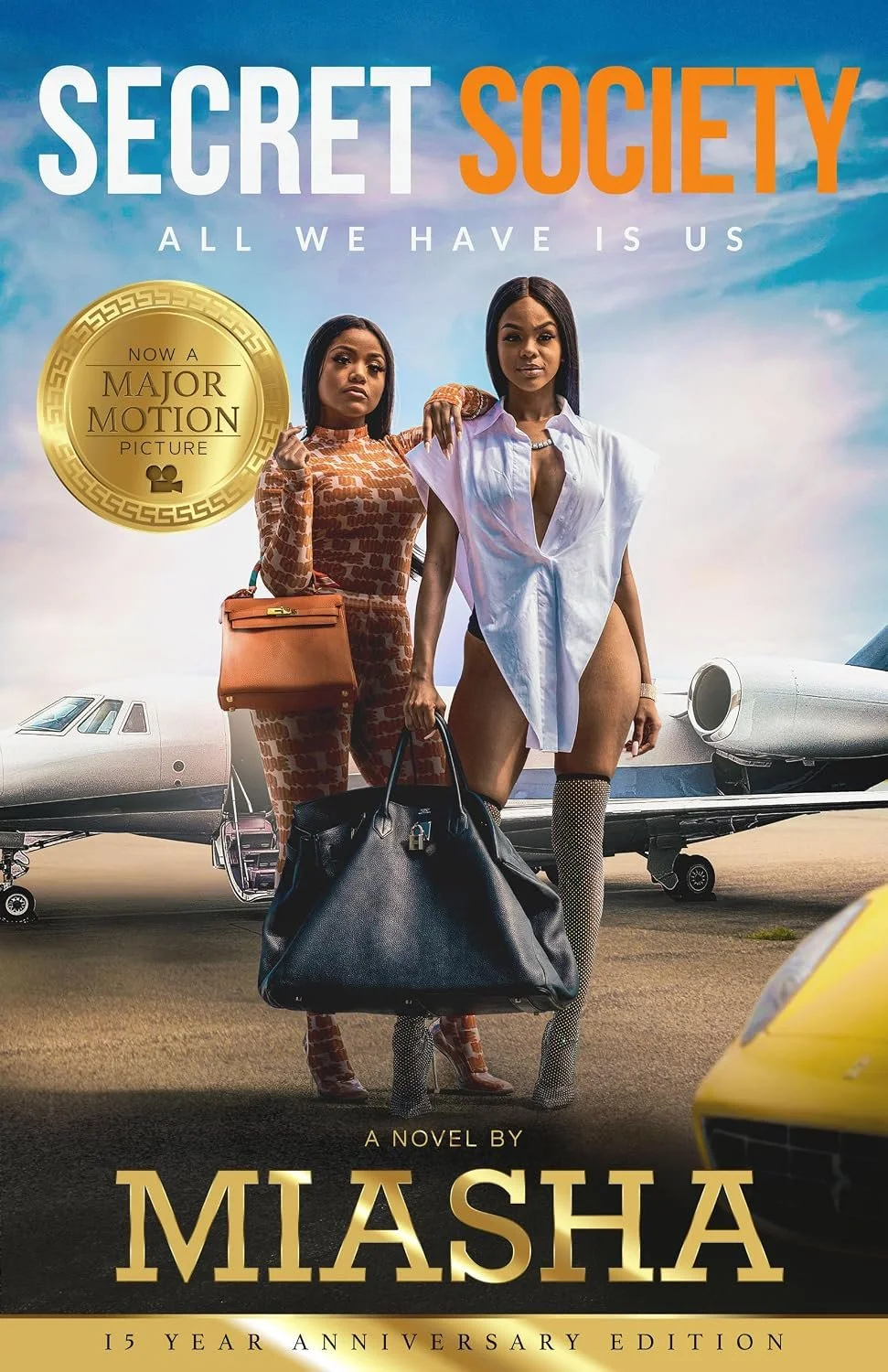 Book cover for "Secret Society: All We Have is Us" by Misha, featuring two women standing in front of private jets, one wearing a patterned outfit with a handbag and the other in a revealing white shirt and fishnet stockings, with a clear sky background.
