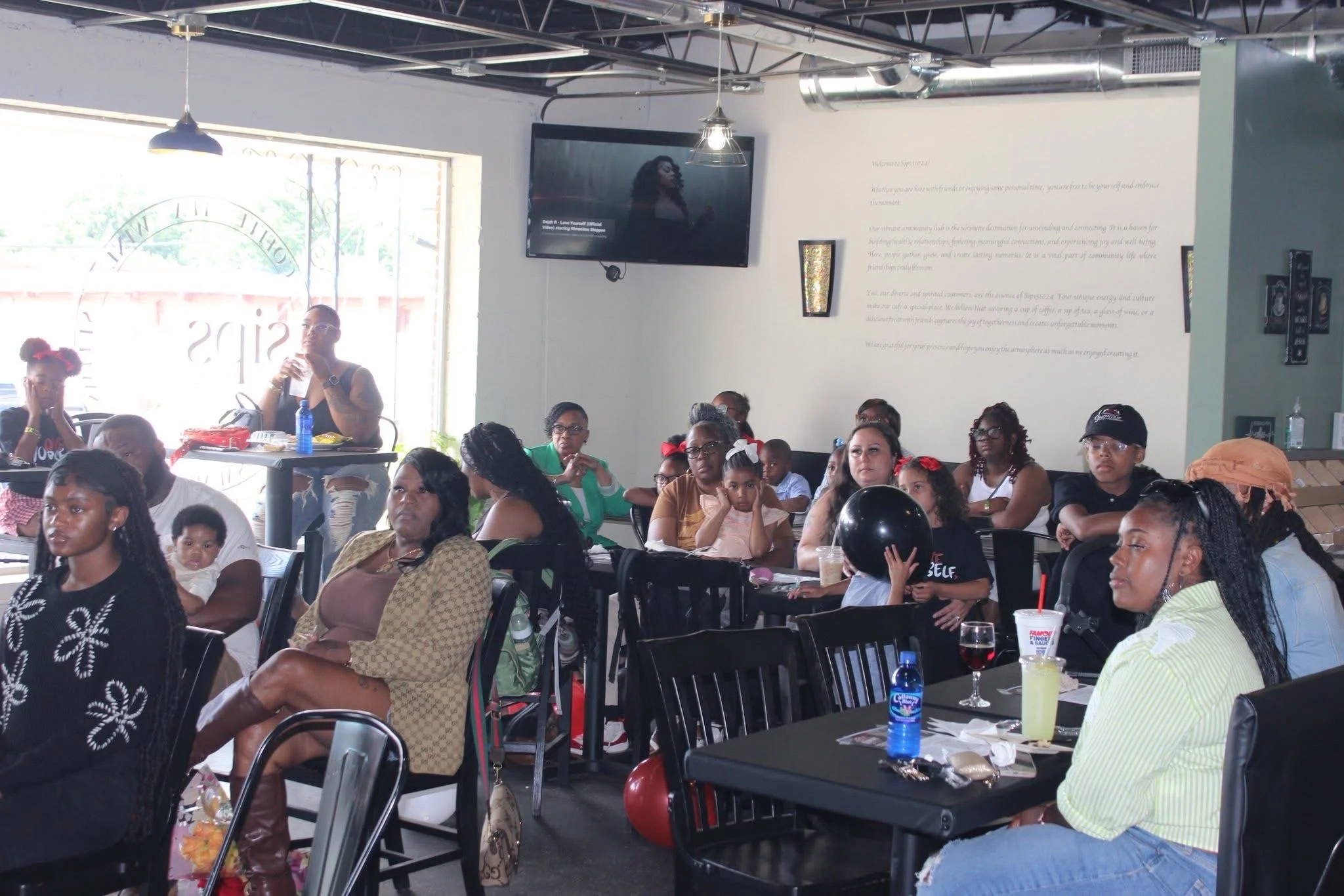 A group of women and children sitting and listening at a social event or gathering in a restaurant or café.