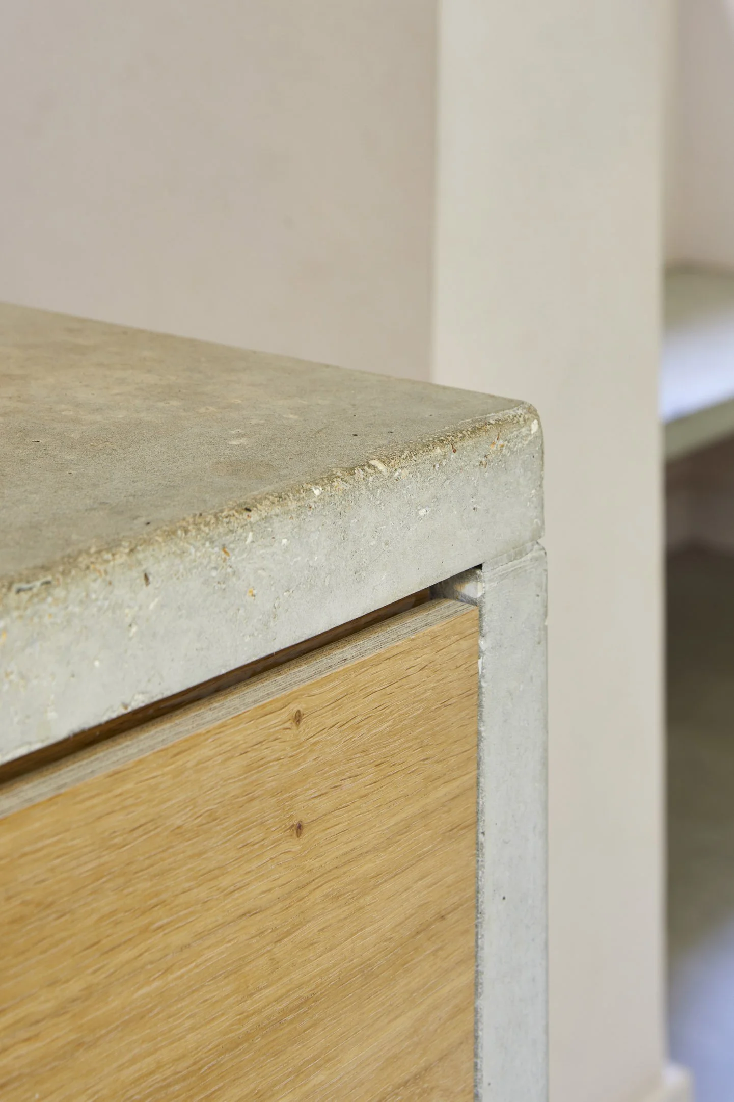 Detail view of the kitchen island combining polished concrete surfaces with warm timber cabinetry and muted finishes.