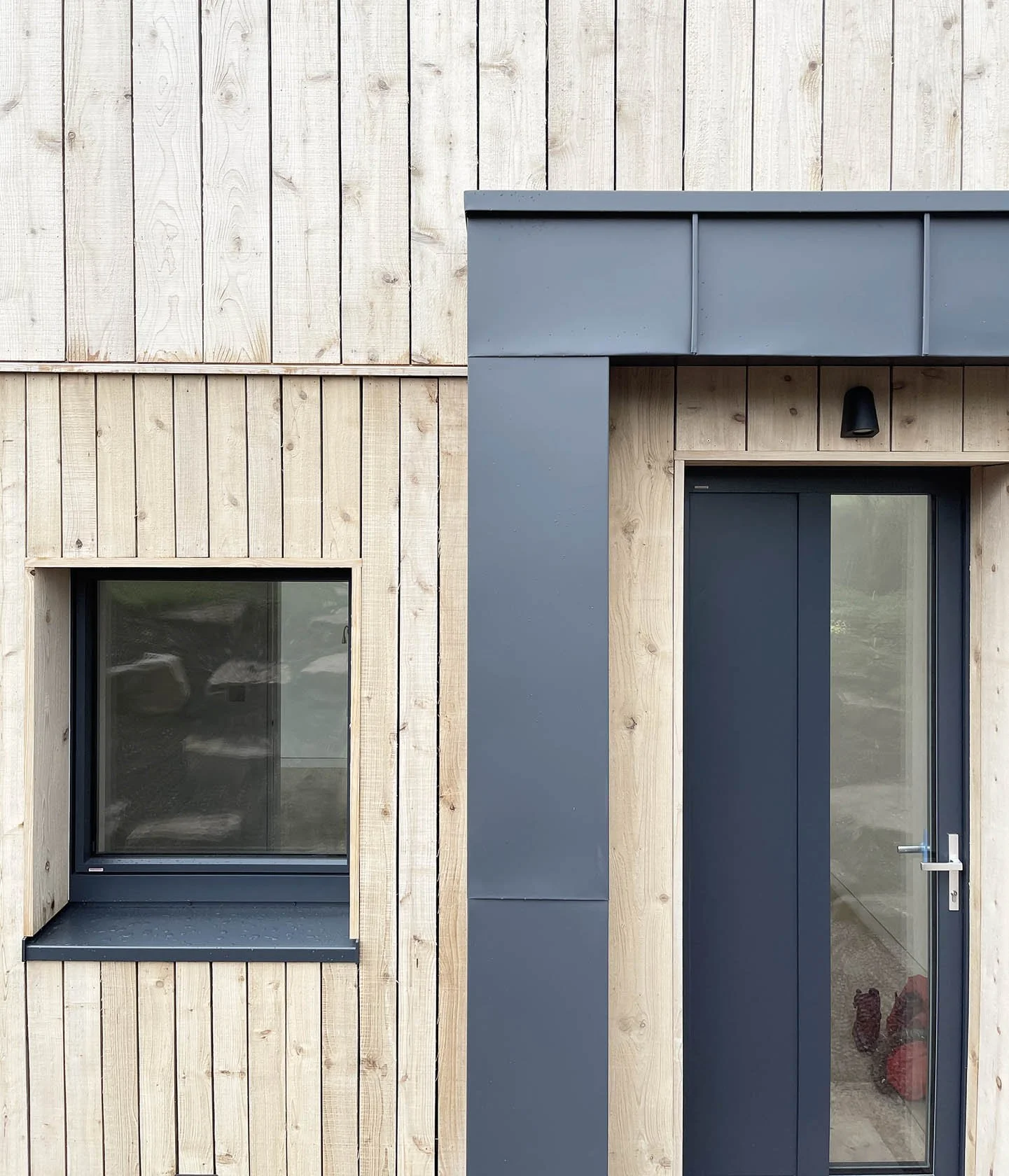 Close-up view of The Sunny House exterior showing the junction between timber cladding and standing seam metal roofing, highlighting the refined material detailing and the building’s calm, durable expression within the valley landscape.