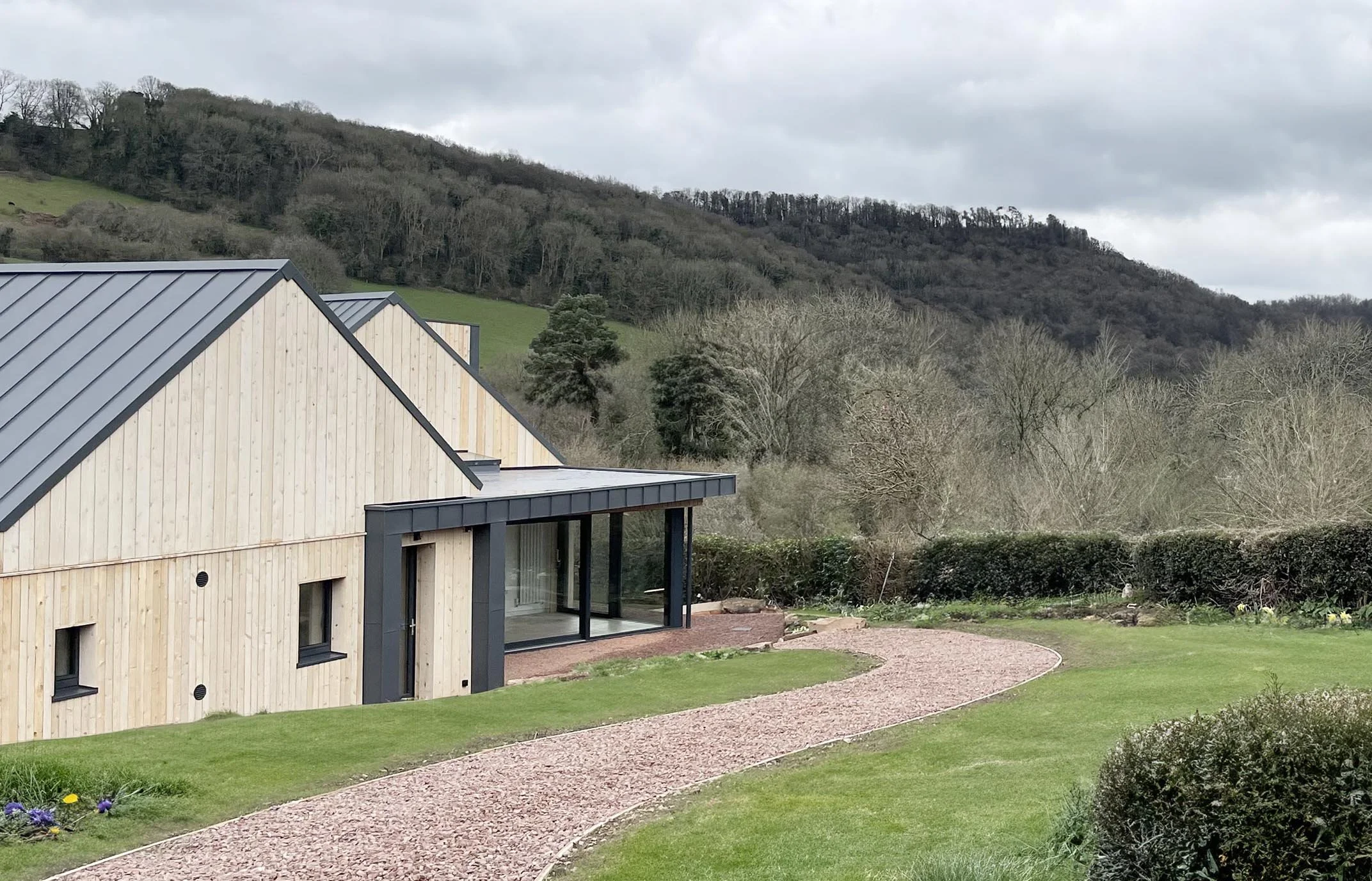 Exterior view of The Sunny House set in the Lower Wye Valley, showing two cranked gabled forms sitting quietly within the rural landscape.