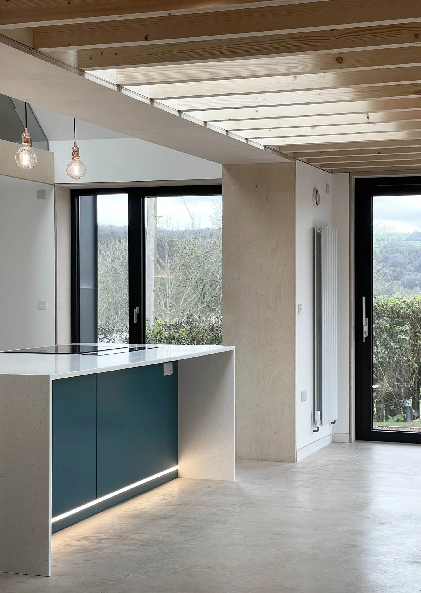 Kitchen and dining space in The Sunny House, set within an exposed timber structure that expresses the roof form and brings warmth and rhythm to the double-height interior.