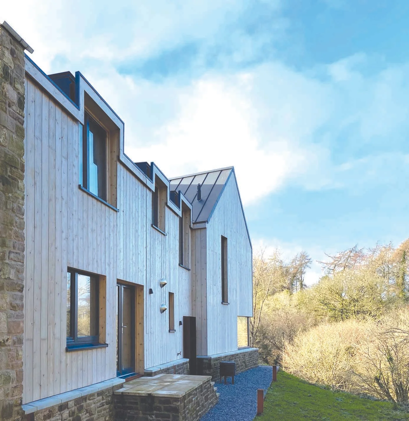 Detail of the façade materials under changing daylight, highlighting the subtle textures and weathering qualities that allow the building to blend gently with its rural setting.