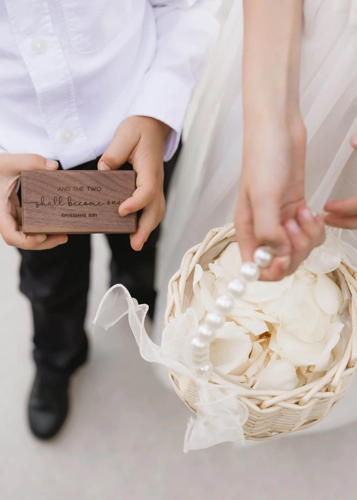 Close-up of a couple holding a small wooden box with a Bible verse, and a basket filled with rose petals, during a wedding ceremony.