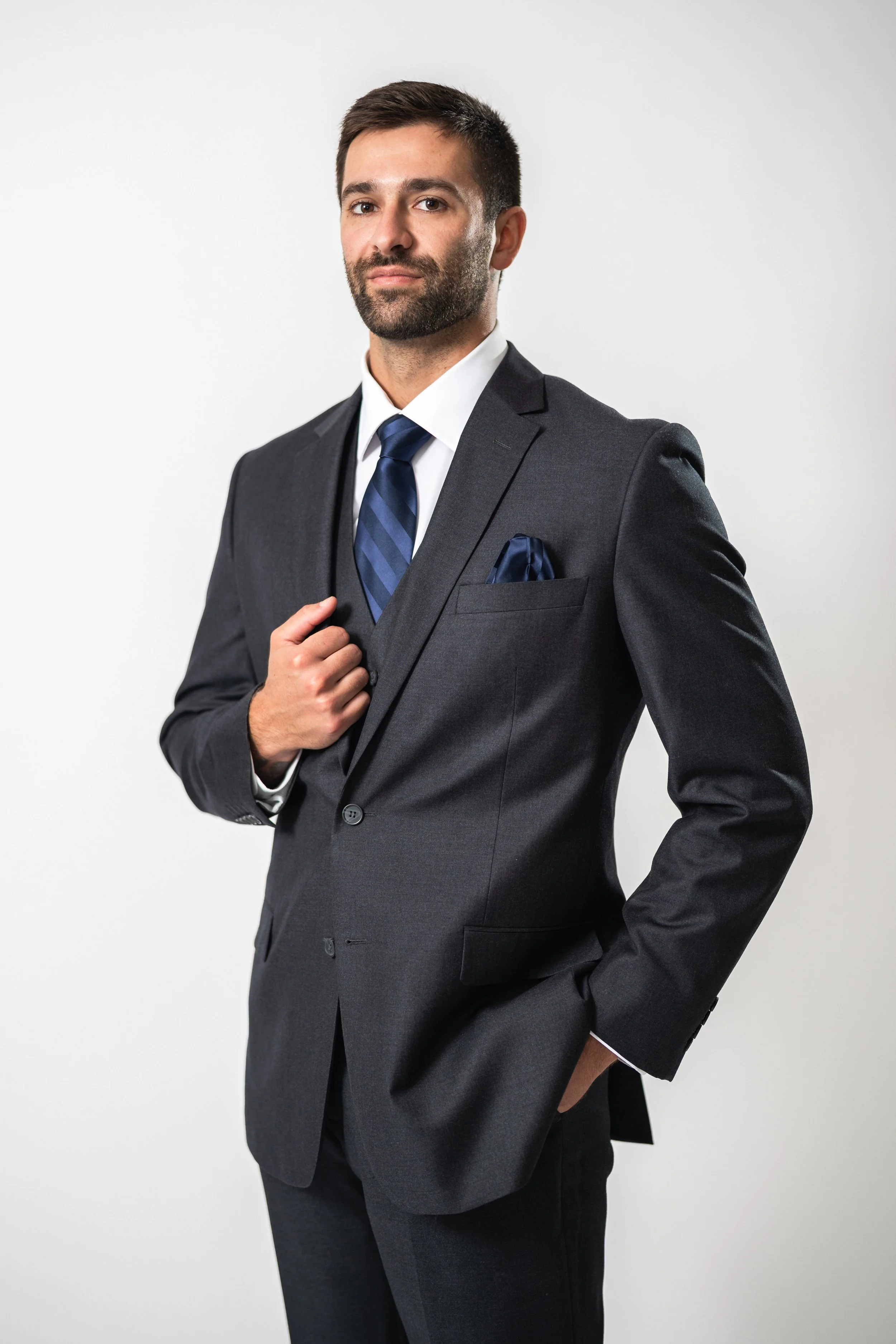 A man in a dark suit with a white shirt and a blue striped tie posing against a plain white background.