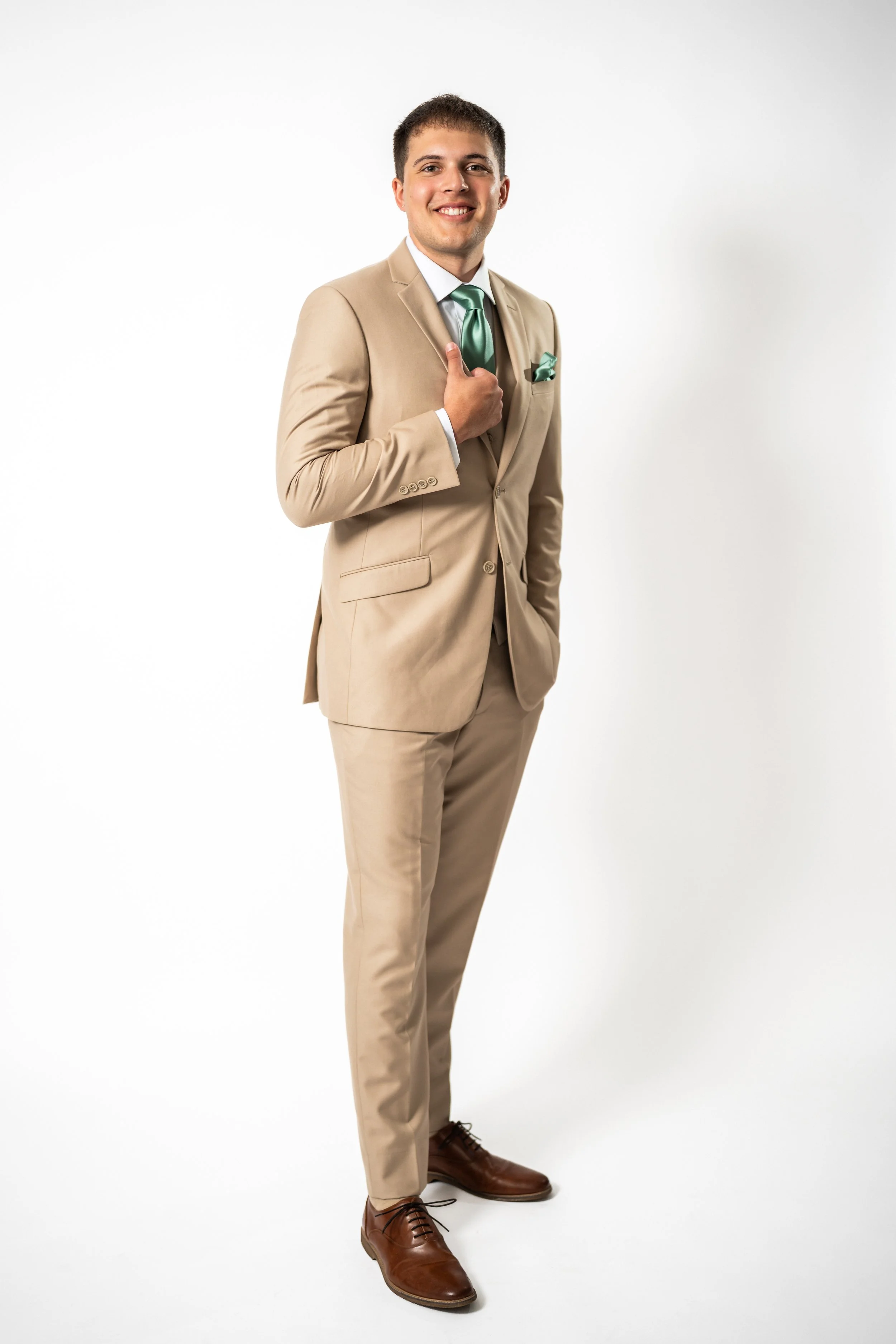 A smiling man in a beige suit with a green tie standing against a white background.