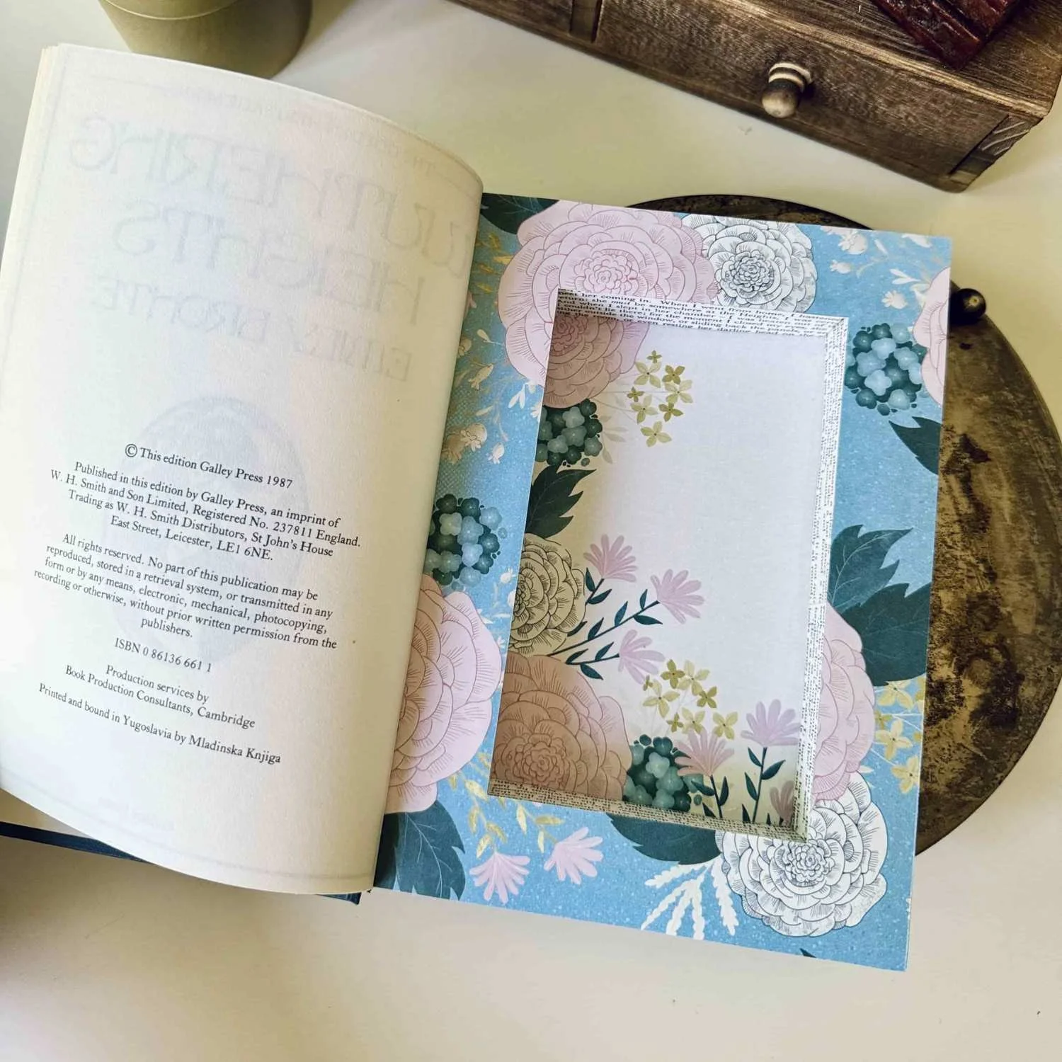 A hollow book made into a decorative floral storage box lying on a white table.