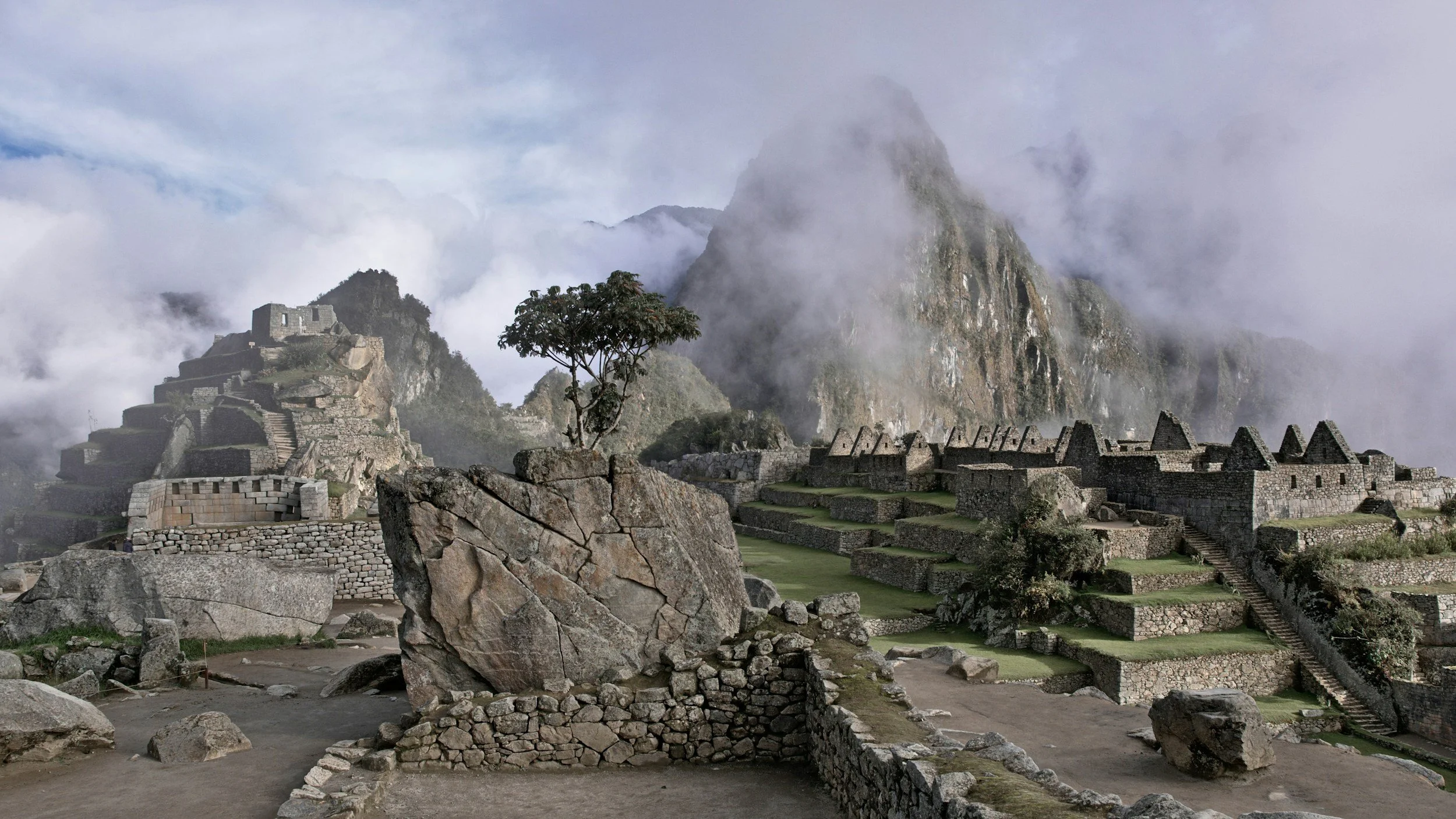 Ancient ruins at Machu Picchu surrounded by mountains and clouds, with terraces and stone structures, in Peru.