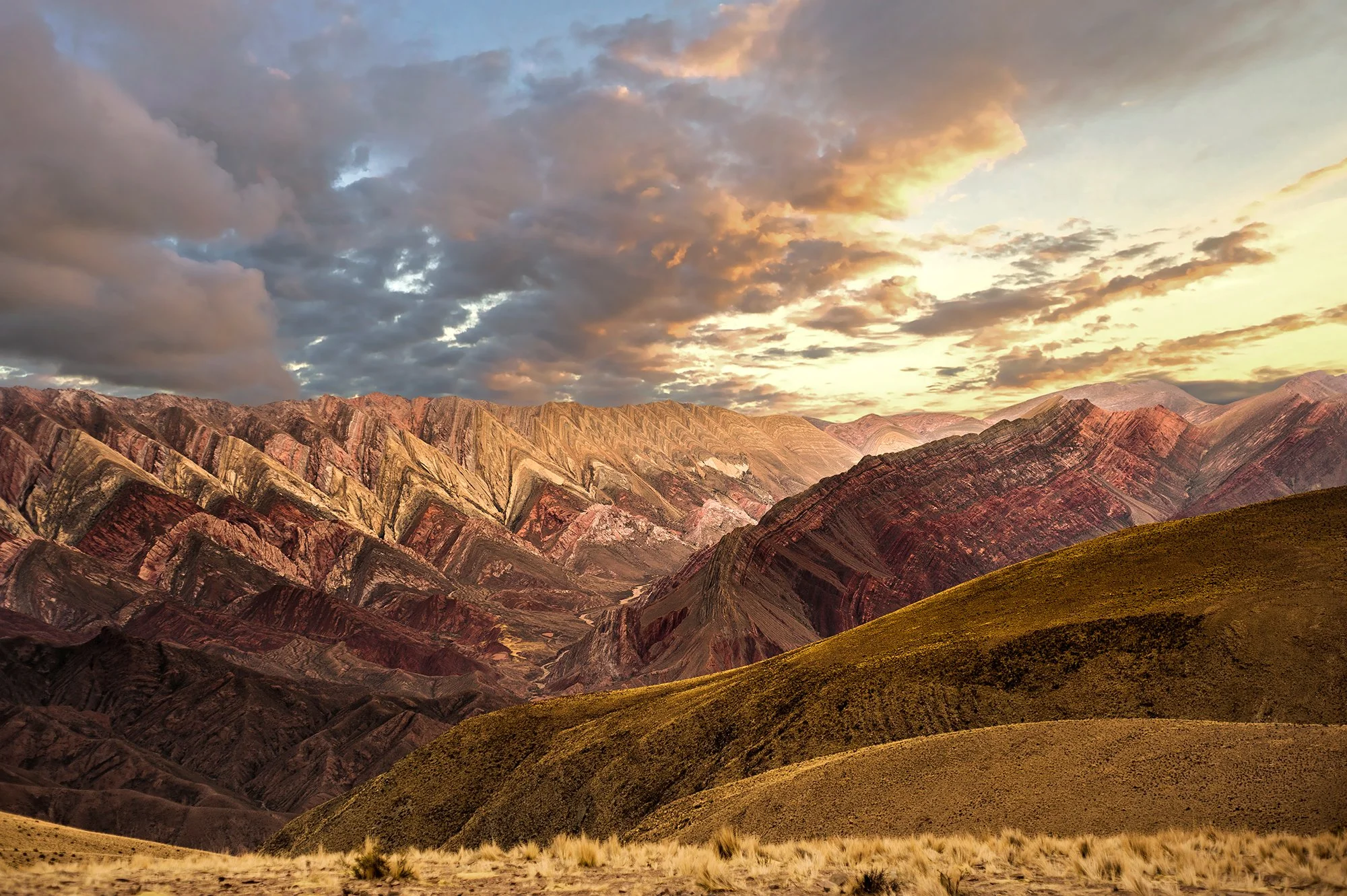 Colorful mountain landscape at sunset with a grassy foreground and cloudy sky