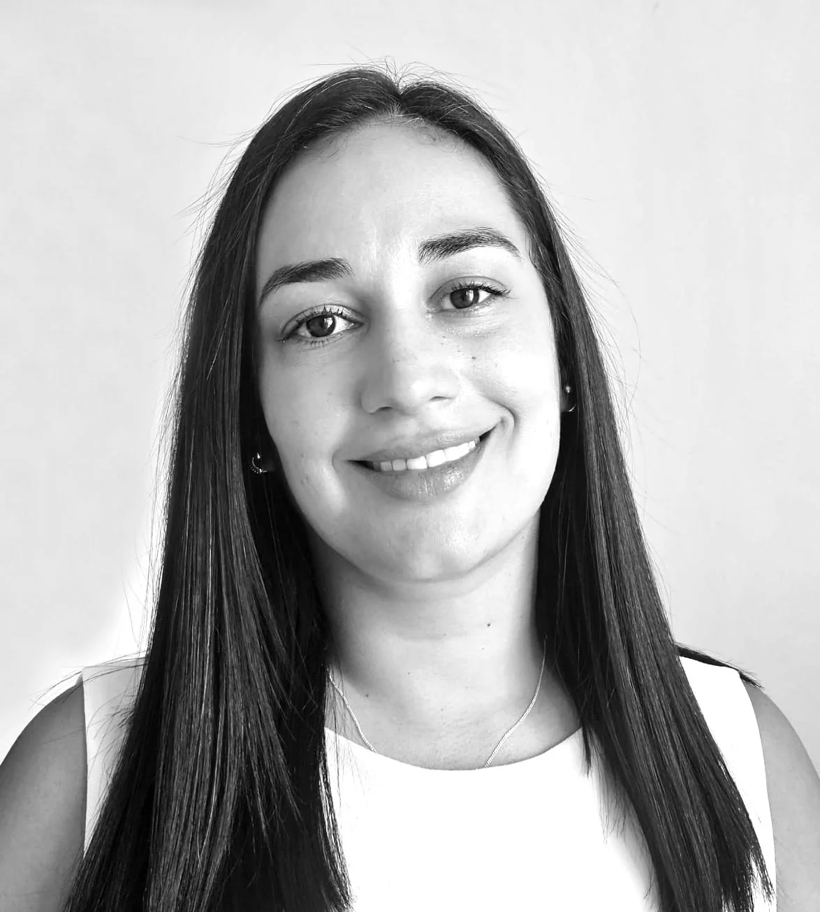 Black and white portrait of a smiling woman with long dark hair, wearing a sleeveless top and a necklace, against a plain background.
