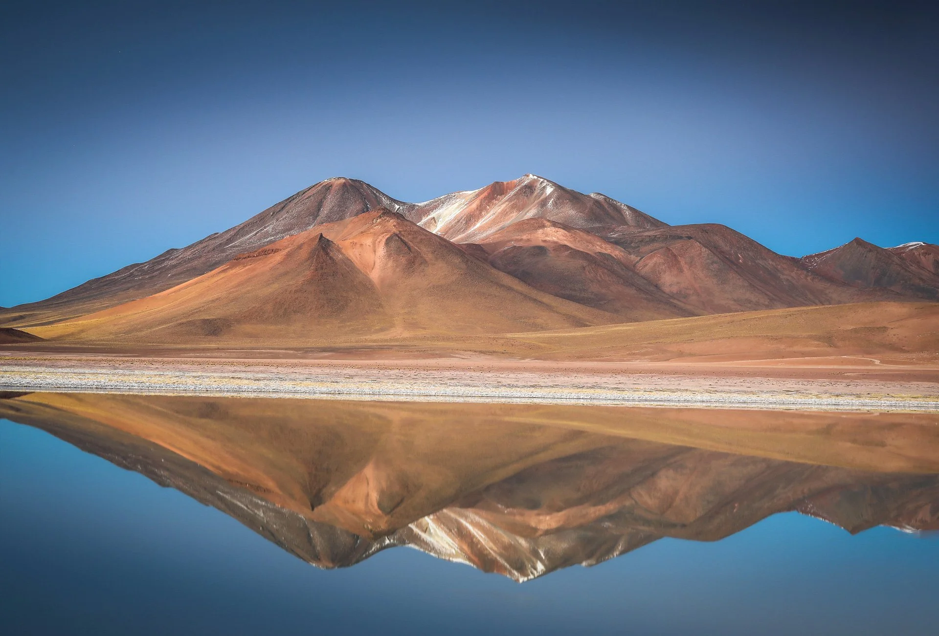 Mountain range with colorful peaks reflected in a lake with a clear blue sky. San Pedro, Atacama desert, Chile.
