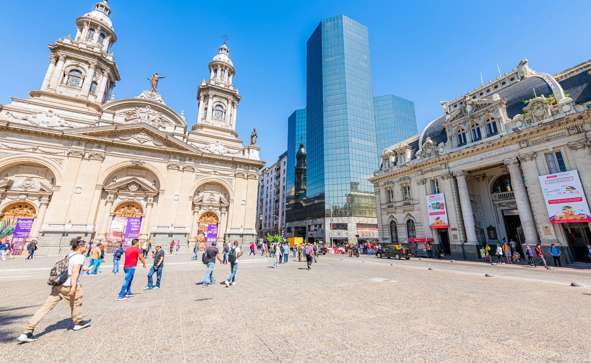 City square with historic church and modern glass skyscraper in the background, people walking and gathering on sunny day, Santiago city Centre, Chile.