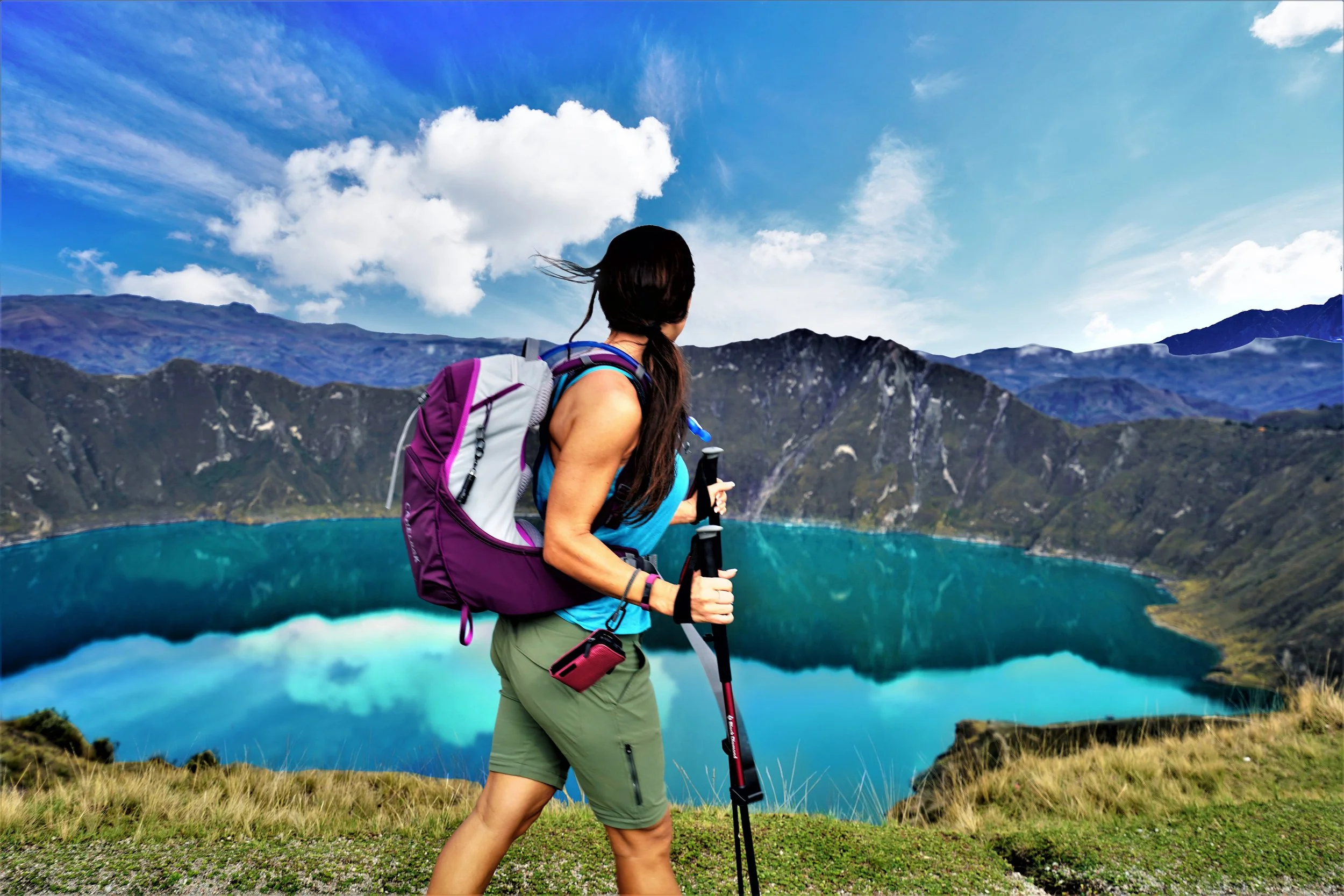 A woman hiking near a lake with mountains in the background under a blue sky with clouds. Ecuador.