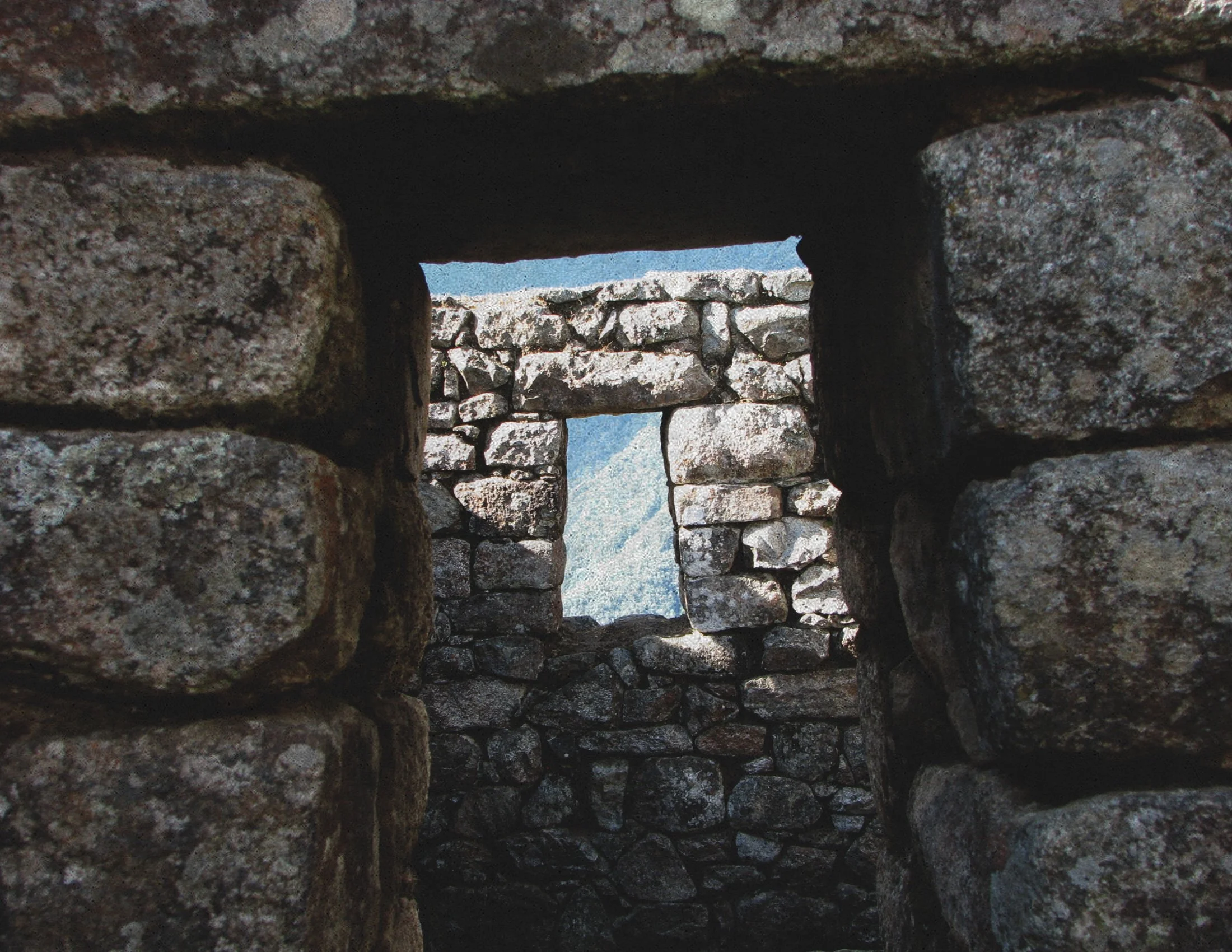 A view through a narrow stone window in an ancient stone structure, Machu Picchu, Peru, with mountains and sky visible in the background.
