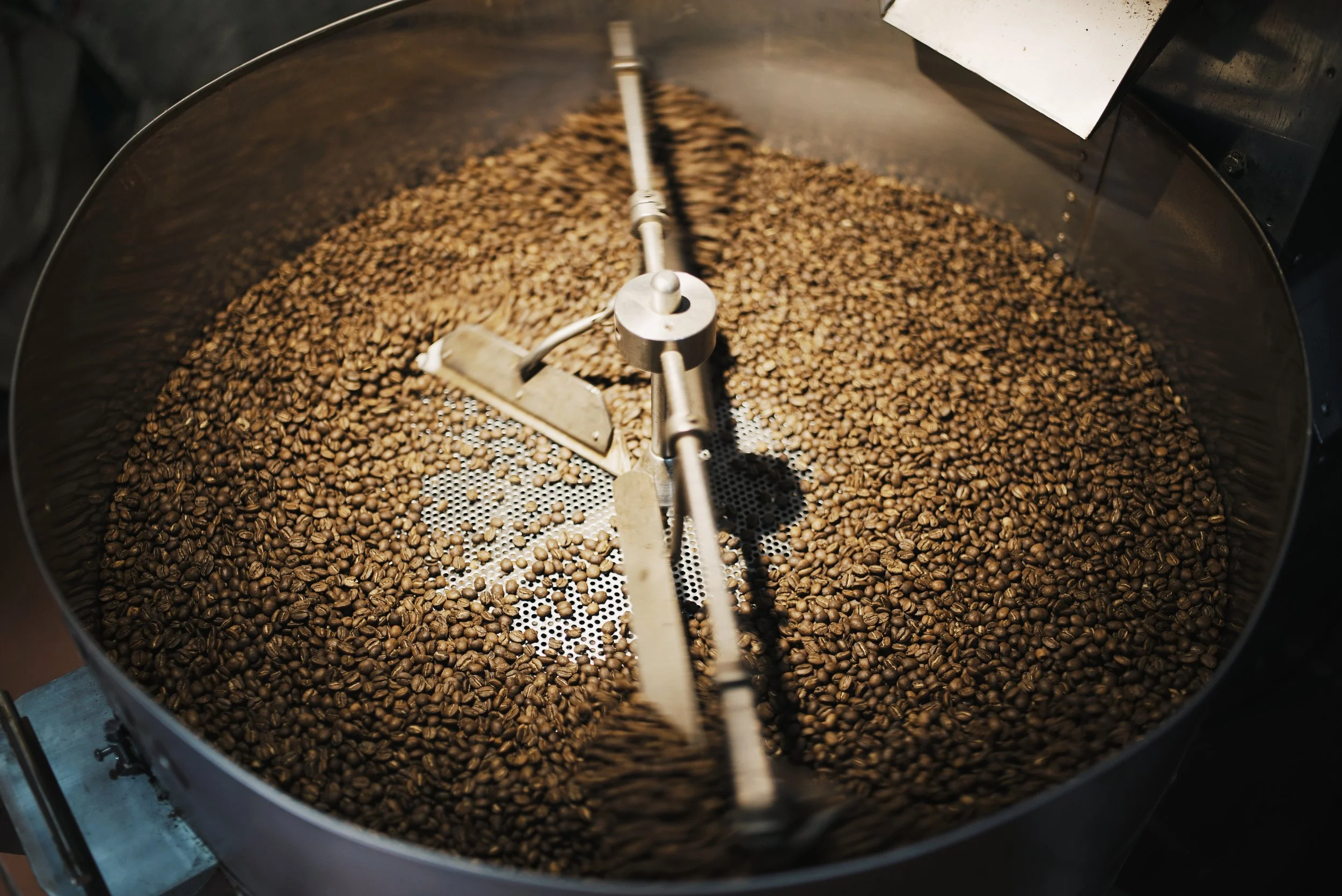 Coffee beans being roasted in a large industrial roaster machine.