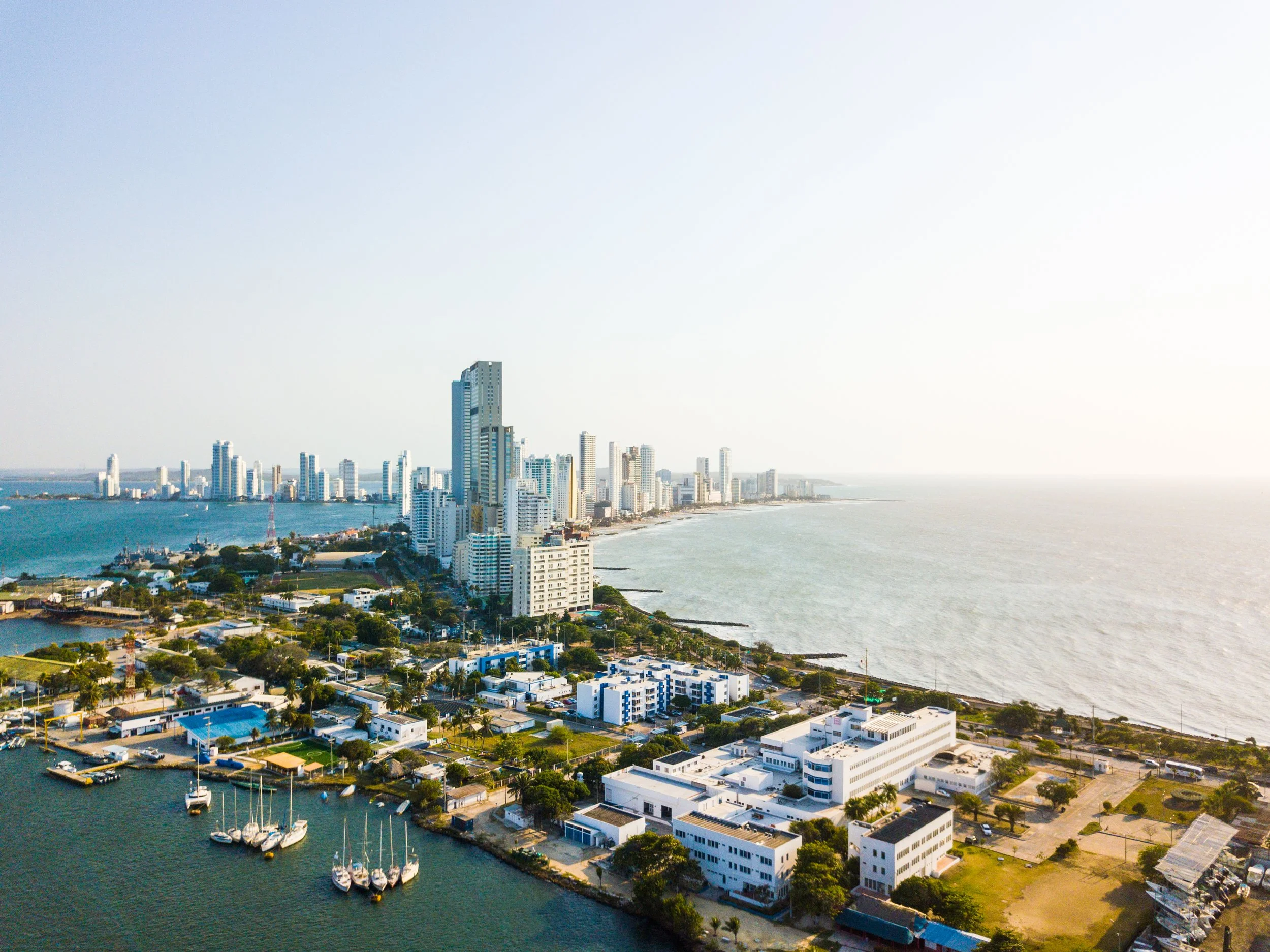 Aerial view of a city skyline along the coast with high-rise buildings, boats in the harbor, and a sandy beach extending into the distance.