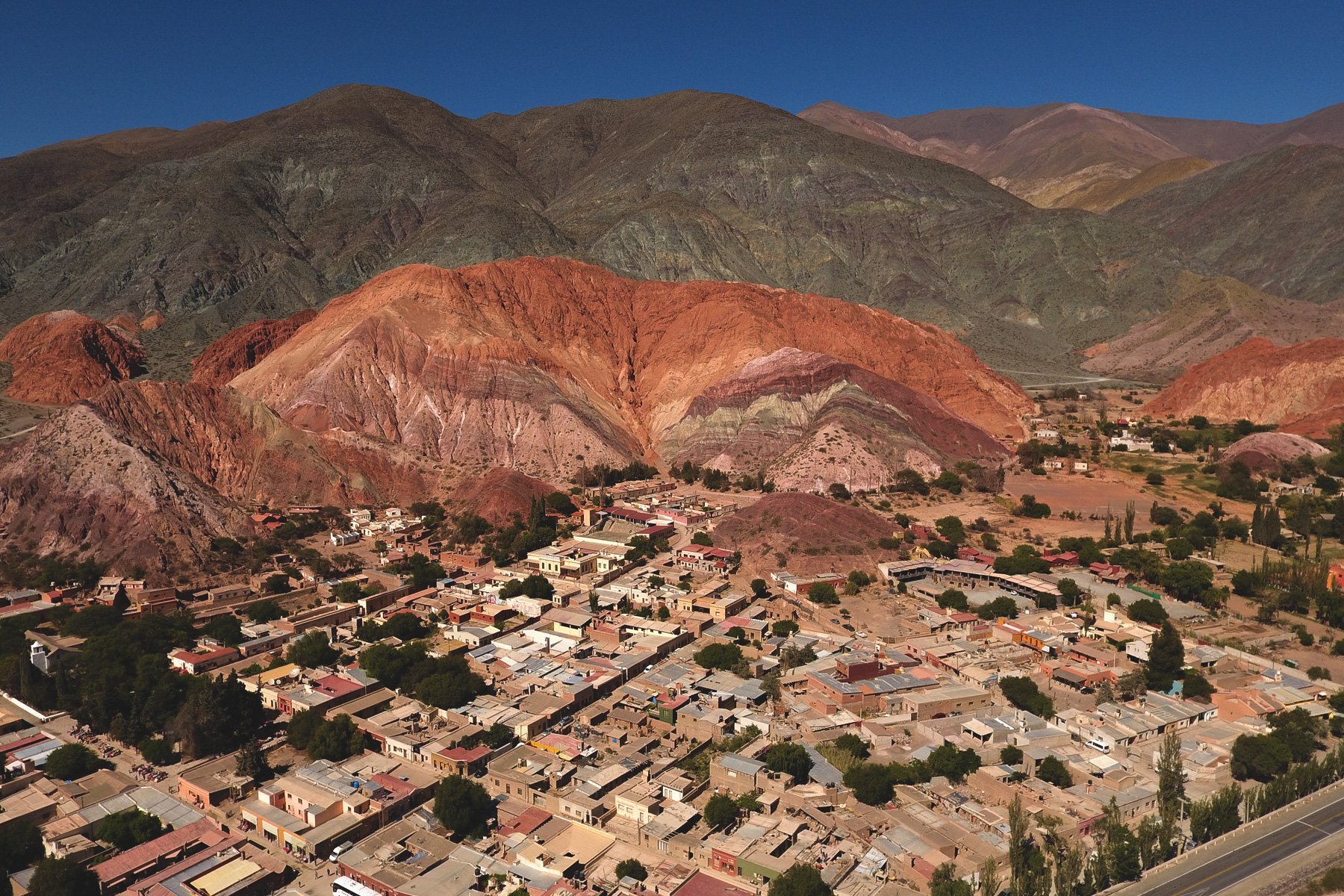 A small town at the base of colorful mountains under a clear blue sky.