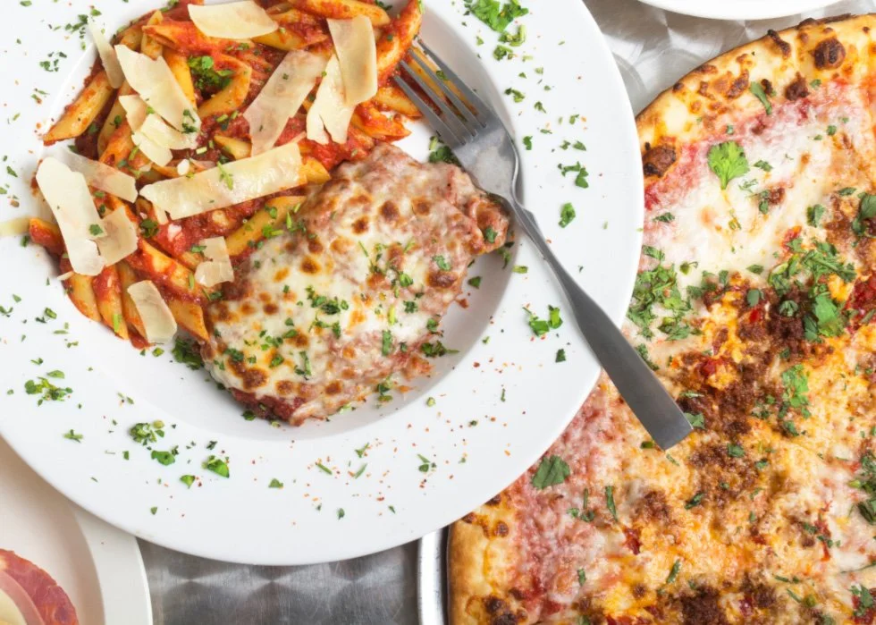 Plate of pasta with marinara sauce and cheese, garnished with herbs, and a slice of pizza with cheese and herbs on the side.