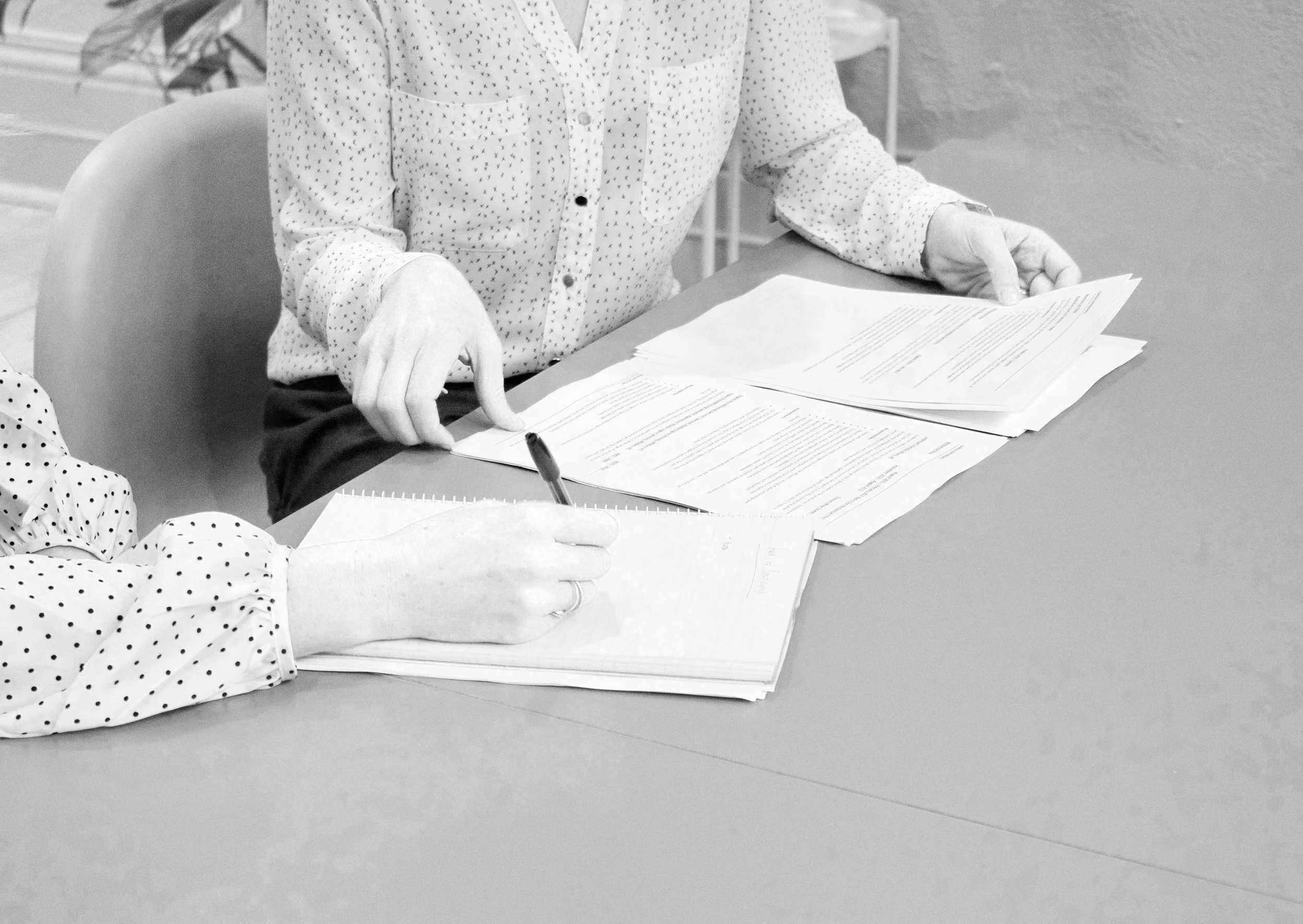 Deux personnes discutent de documents posés sur une table, l'une d'elles écrit sur une feuille, l'autre pointe du doigt vers les documents.