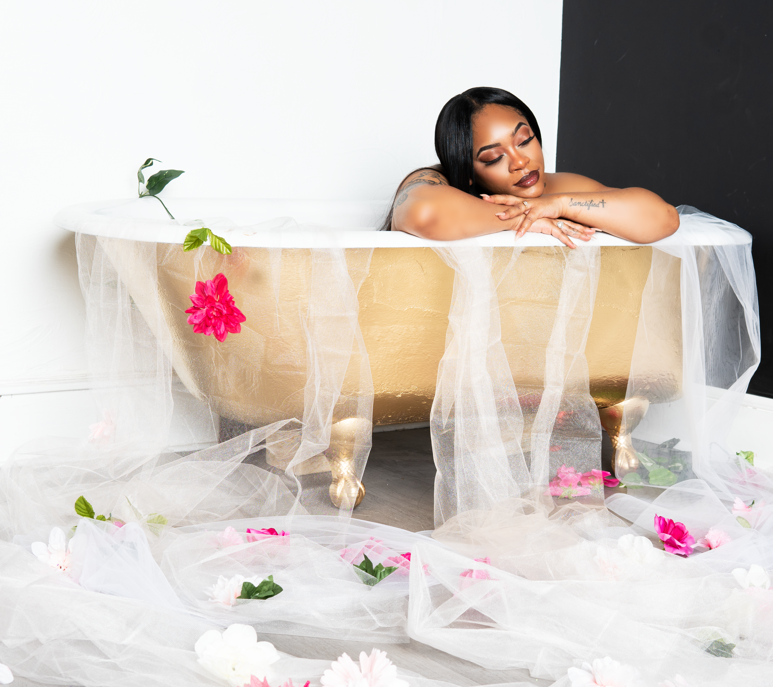 Woman relaxing in a gold bathtub with sheer fabric and flowers